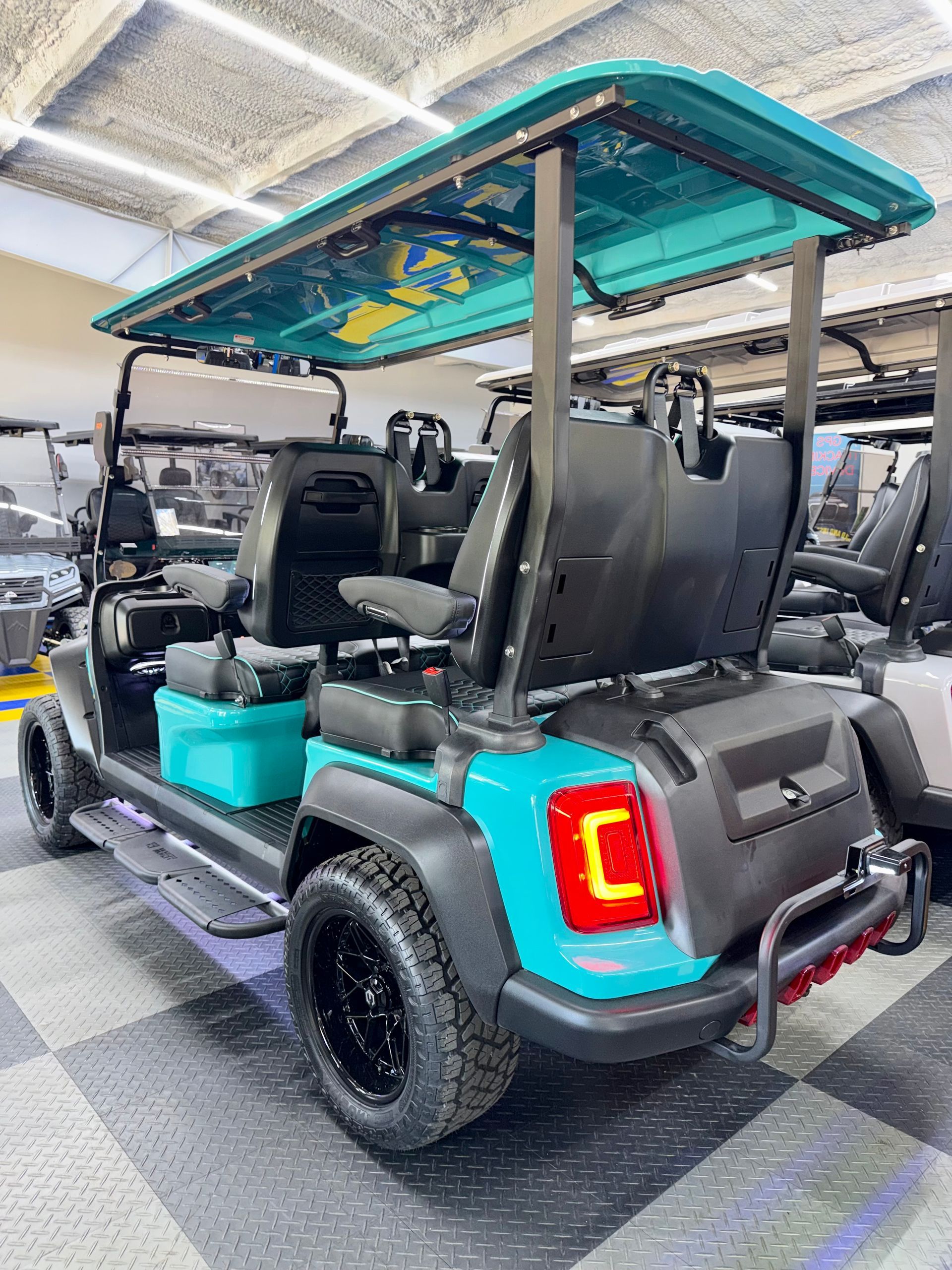 Two-seat golf cart with turquoise trim and roof, parked indoors on a checkered floor