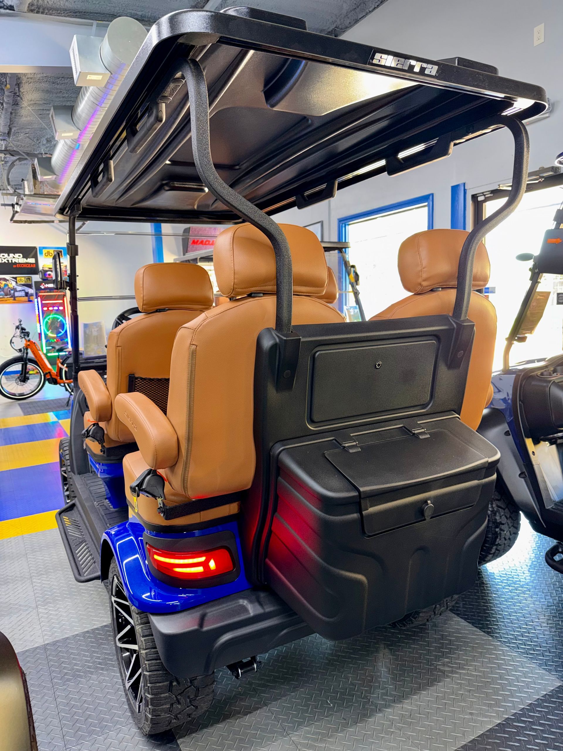 Tan tan 4-seat golf cart with tan seats, black roof, and rear cargo box in a garage showroom