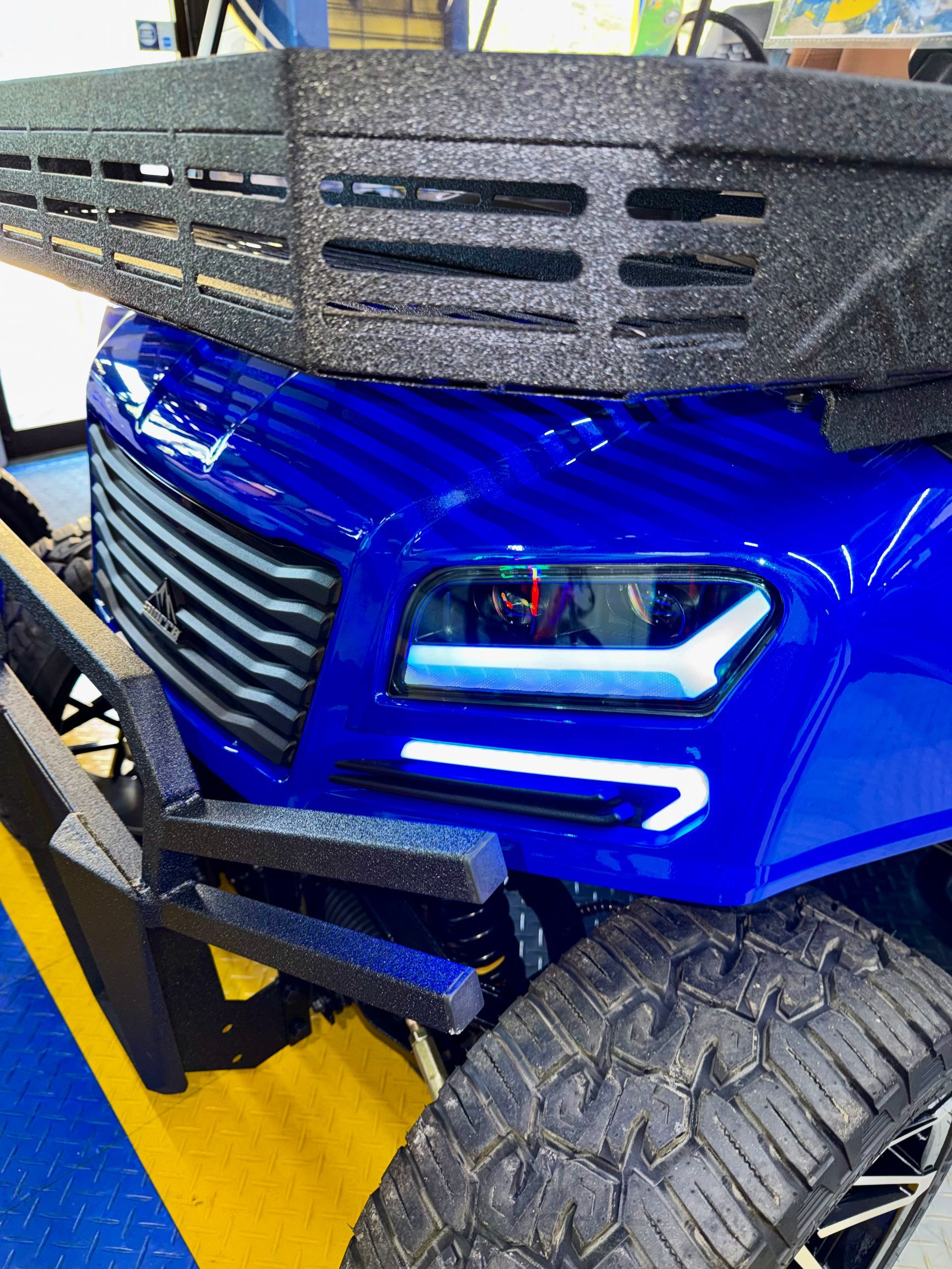 Blue off-road vehicle front end with heavy-duty bumper and roof rack, parked indoors on yellow floor markings