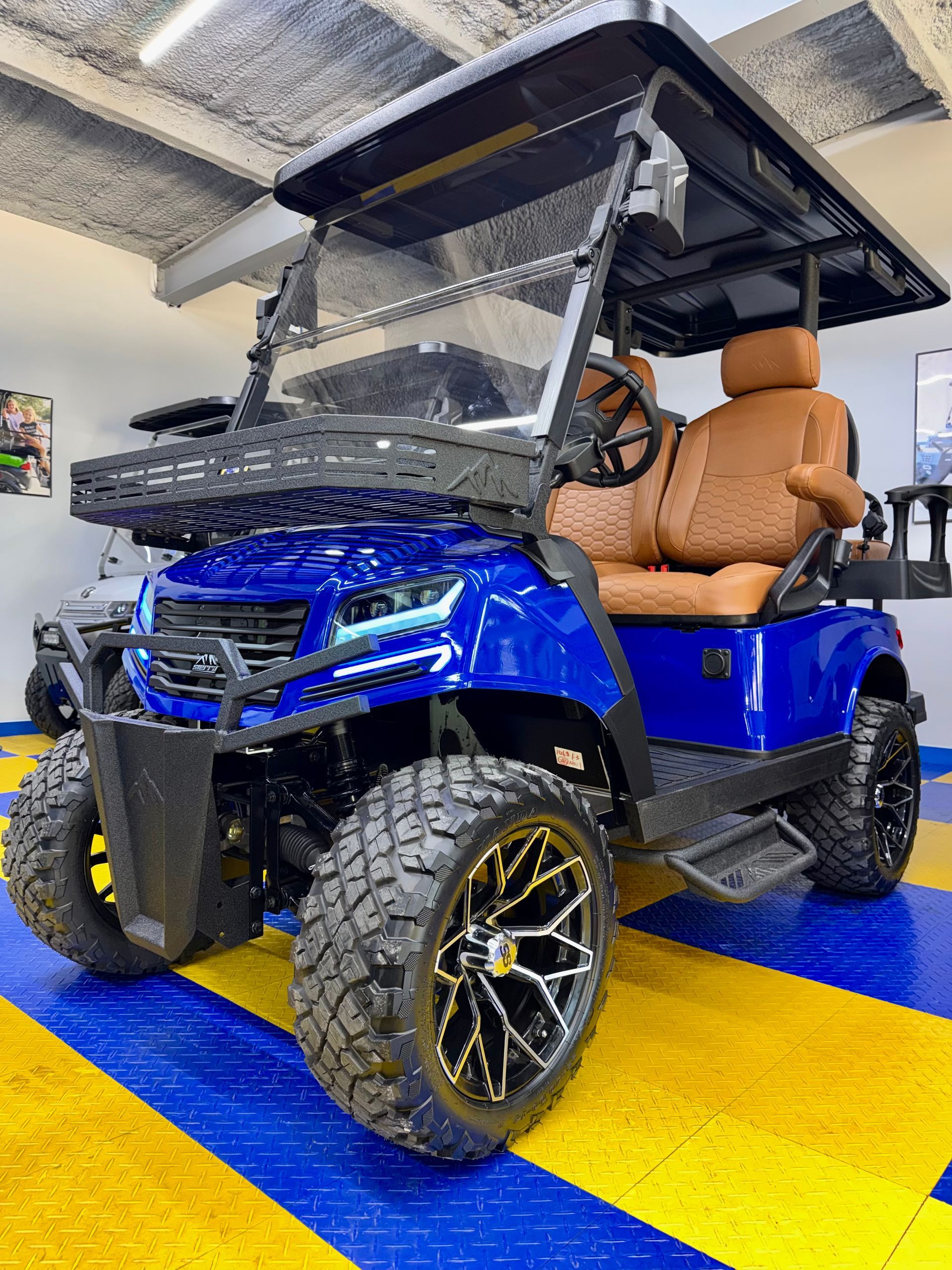 Blue off-road utility vehicle with tan seats and roof, parked indoors on a yellow and blue floor.