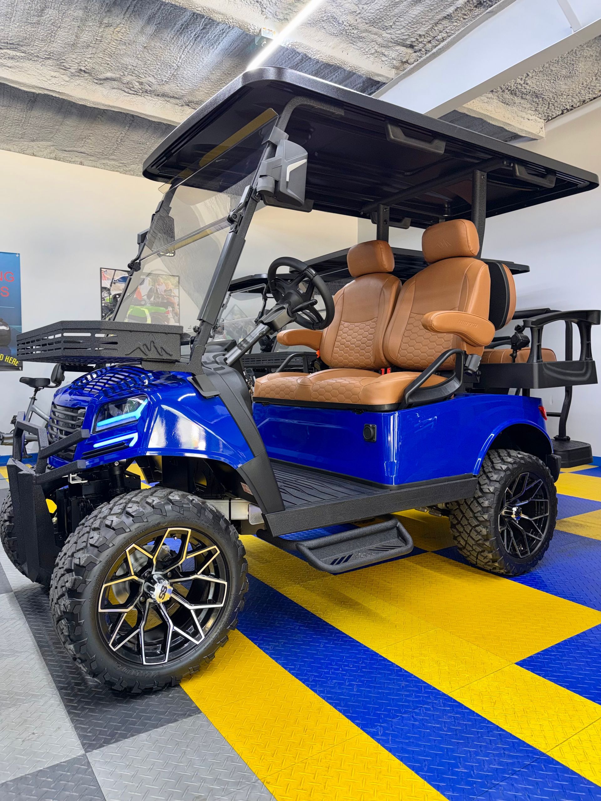 Blue electric golf cart with tan seats parked indoors on yellow and blue floor stripes.