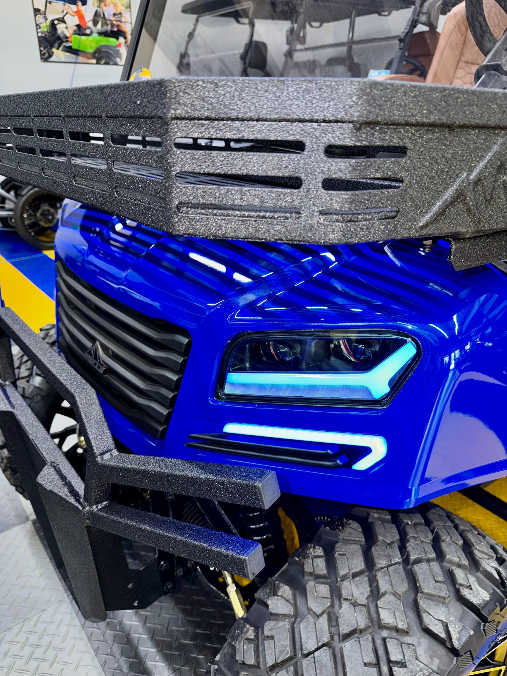 Blue off-road vehicle front with LED headlights and large tire close-up