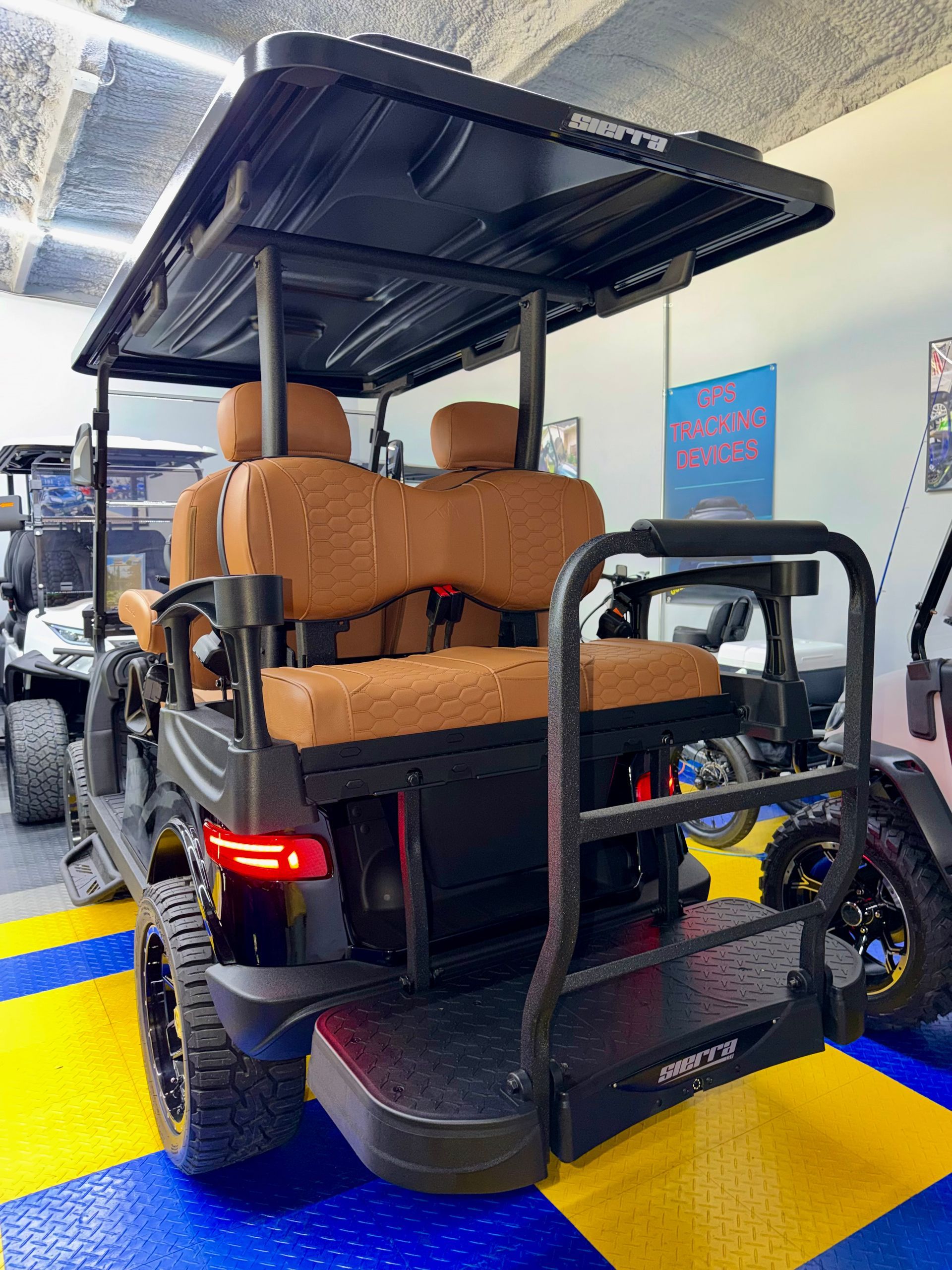 Rear view of a black golf cart with tan seats and roof in a parking area, tail lights on