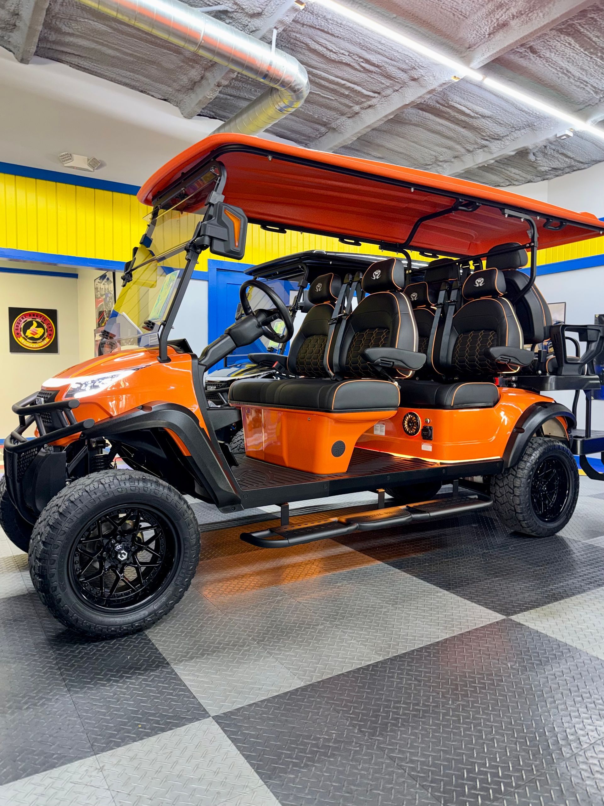 Orange and black golf cart parked indoors under bright lights.