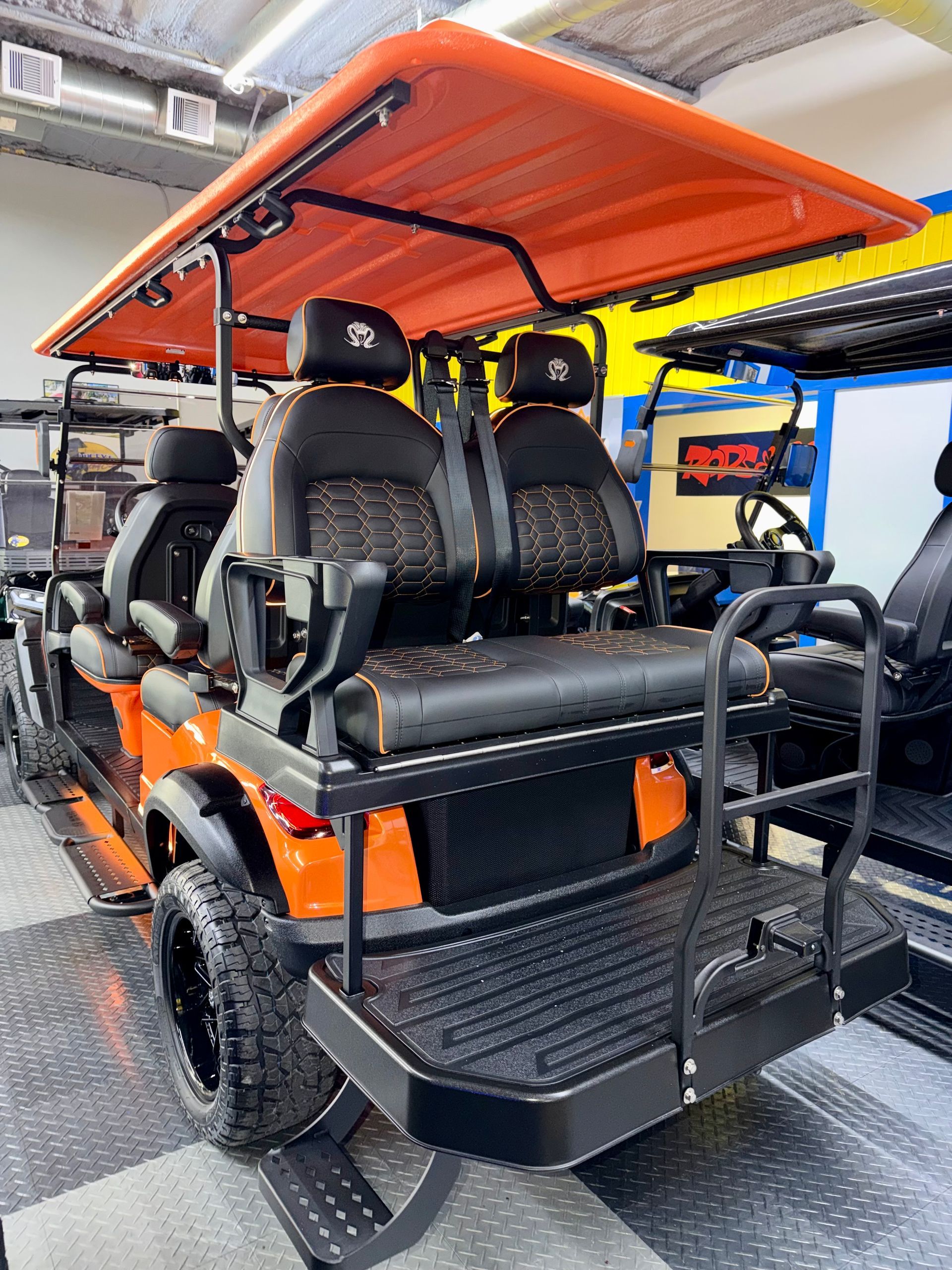 Orange off-road vehicle with black seats and roof, shown from the rear inside a showroom