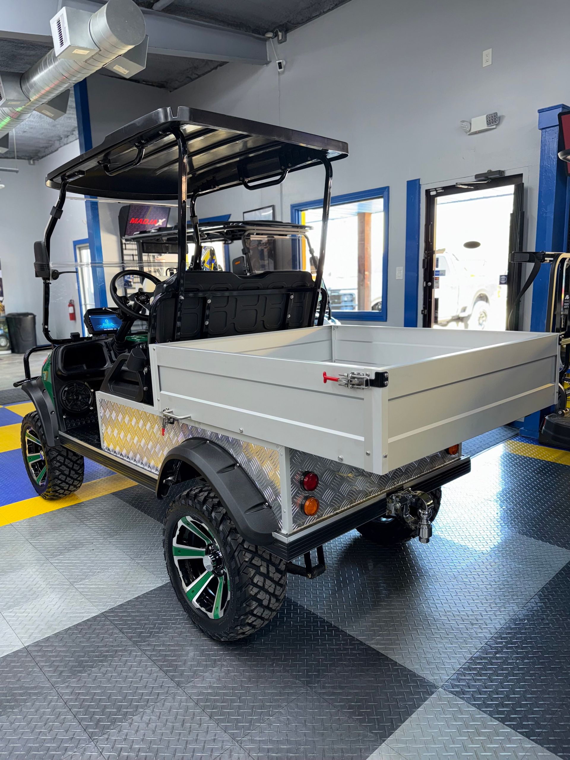 A golf cart with a tray on the back is parked in a garage.