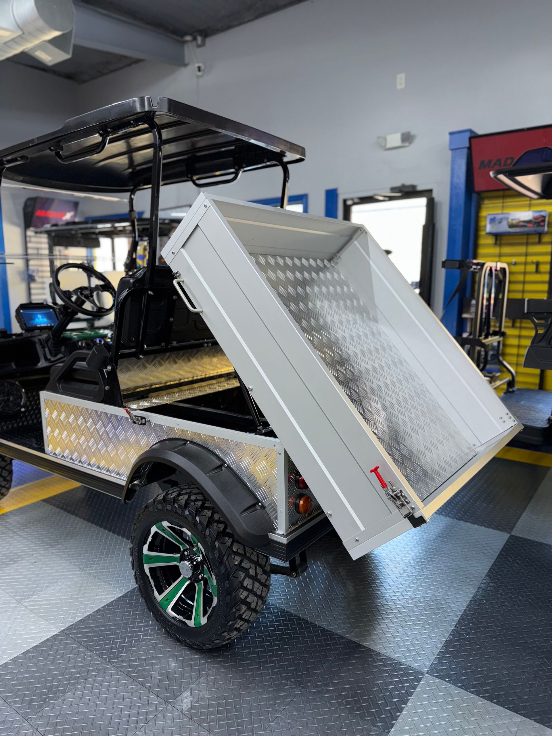 A golf cart with a tray on the back is parked in a garage.