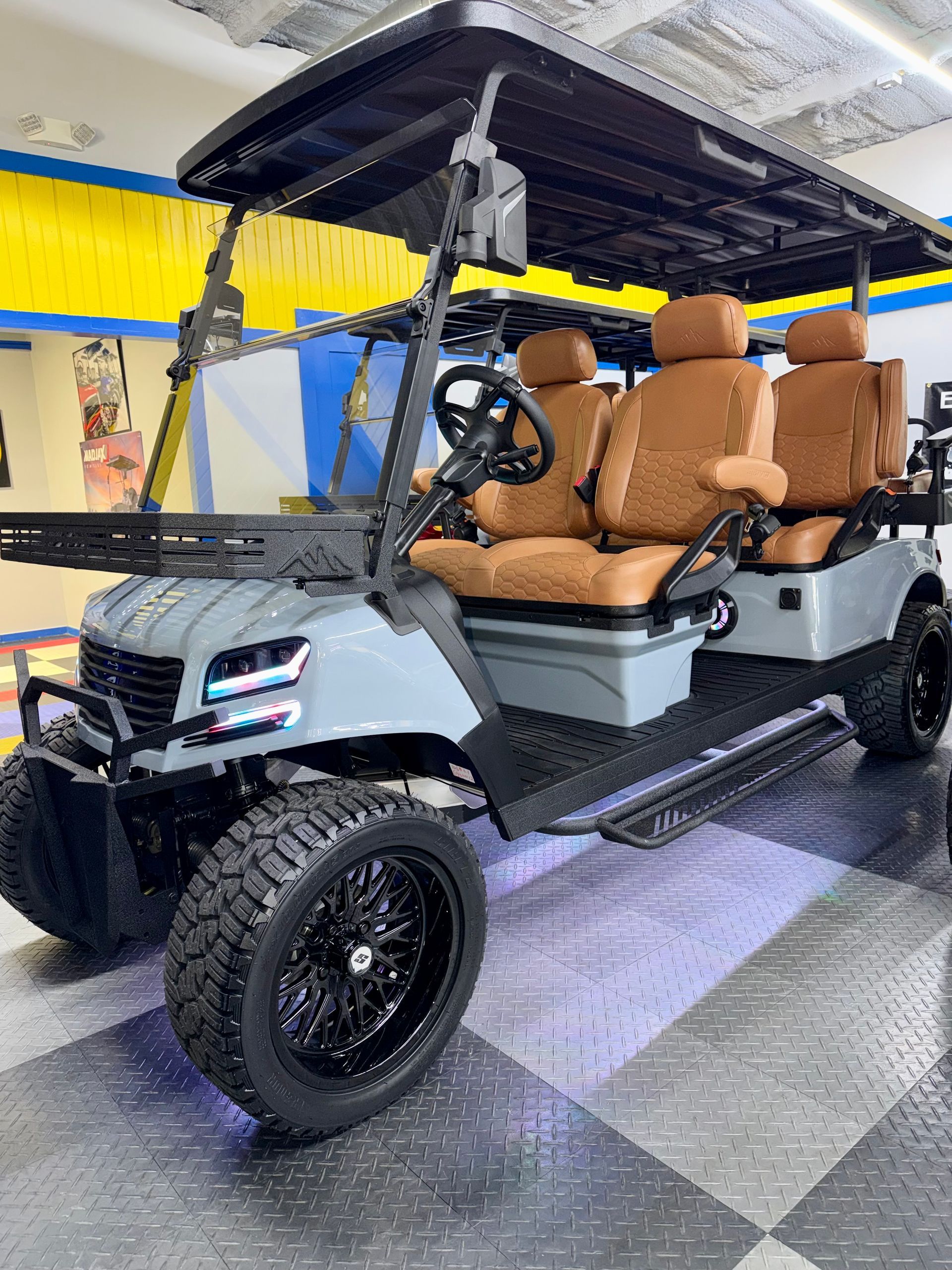 White golf cart with tan seats and roof, shown indoors on a checkered floor.