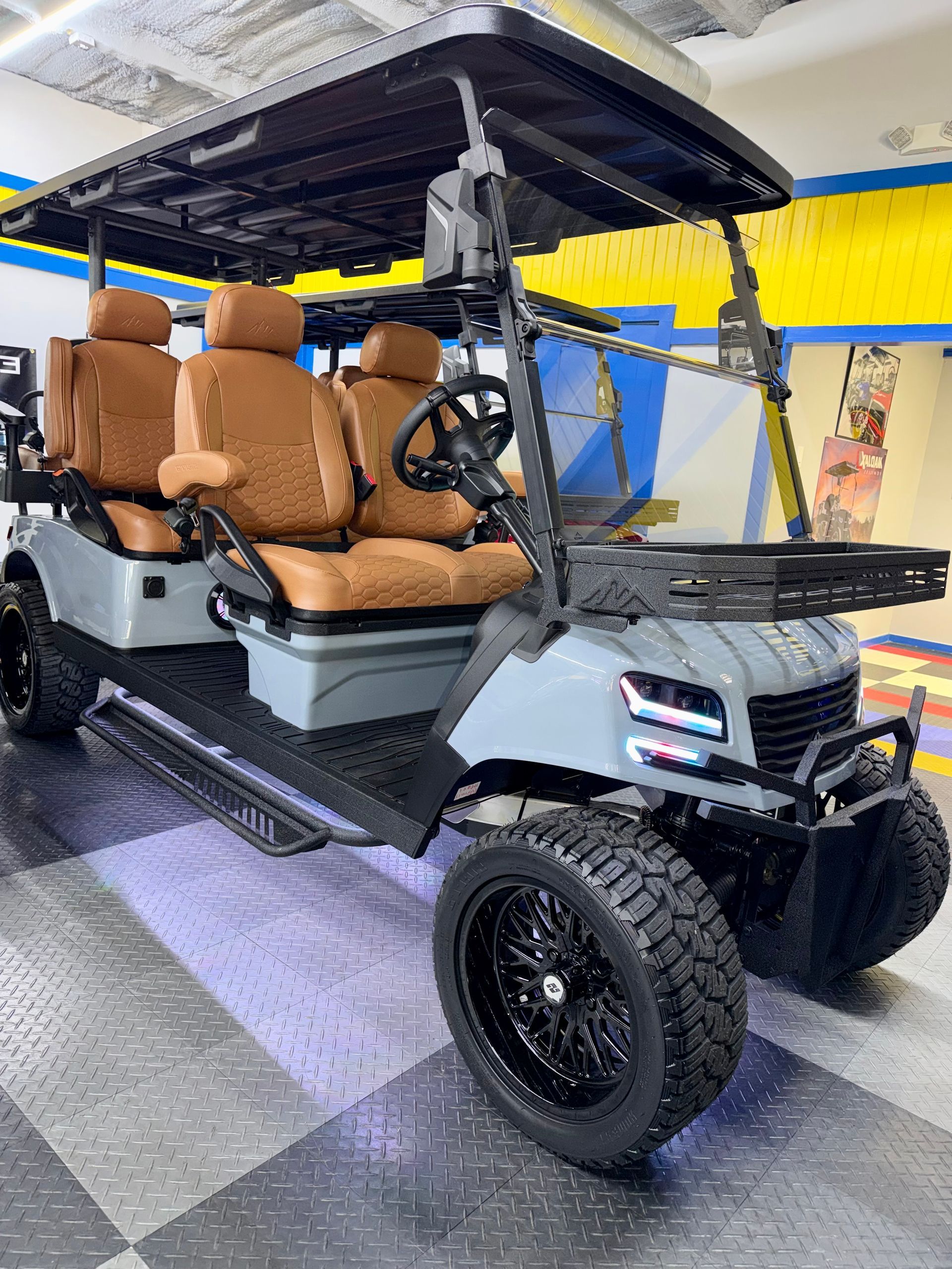 Black off-road golf cart with tan seats and roof, parked indoors on a showroom floor