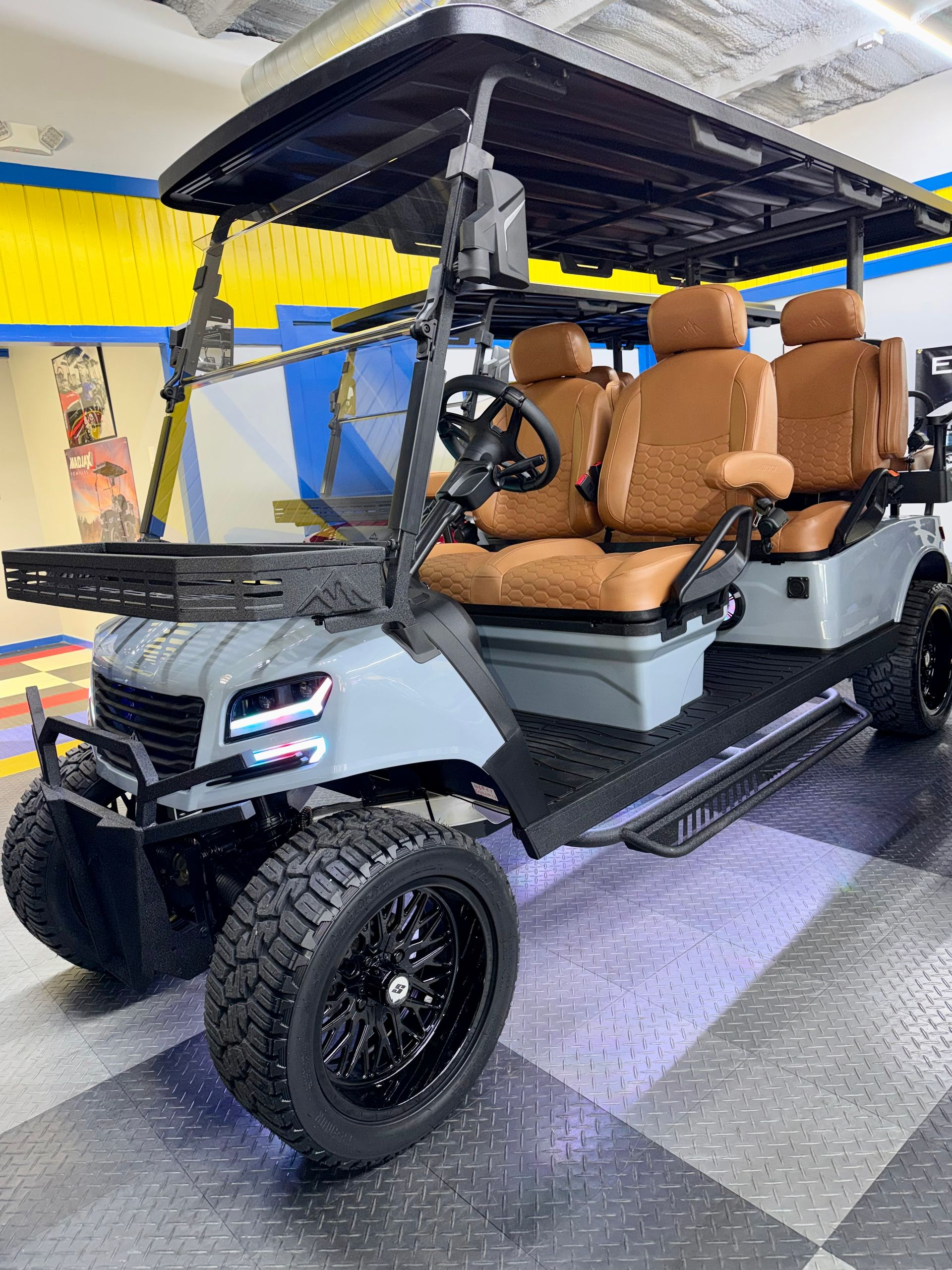 Gray four-seat golf cart with tan seats and roof, parked indoors on a checkered floor.