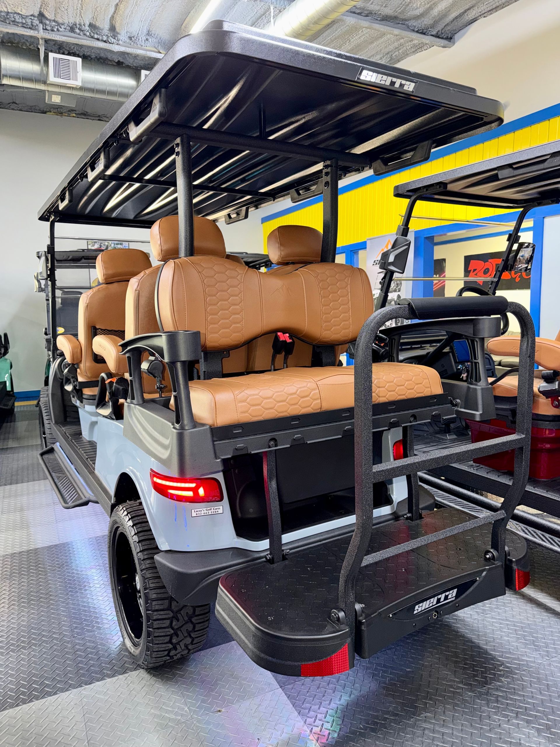 Golf cart with tan seats and black canopy in an indoor garage, rear view.