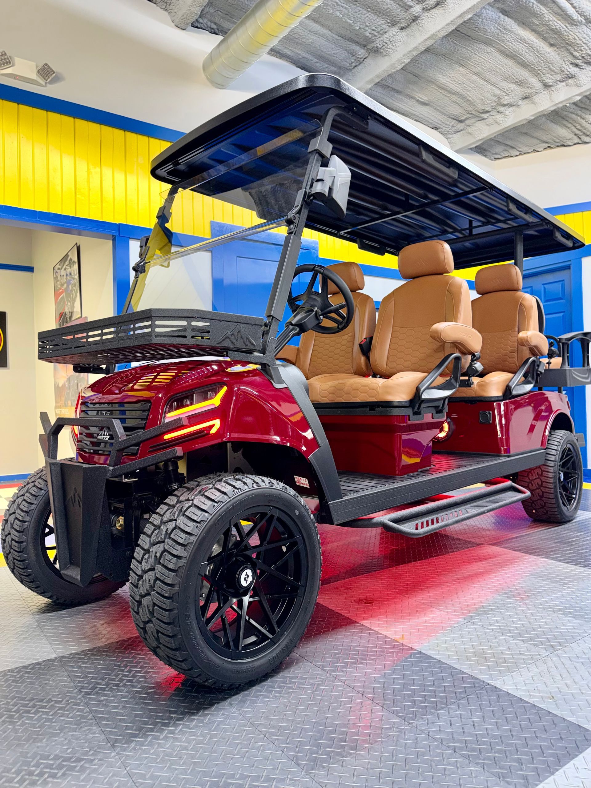 Red four-seat golf cart with roof and tan seats in a showroom, viewed from the front-left.