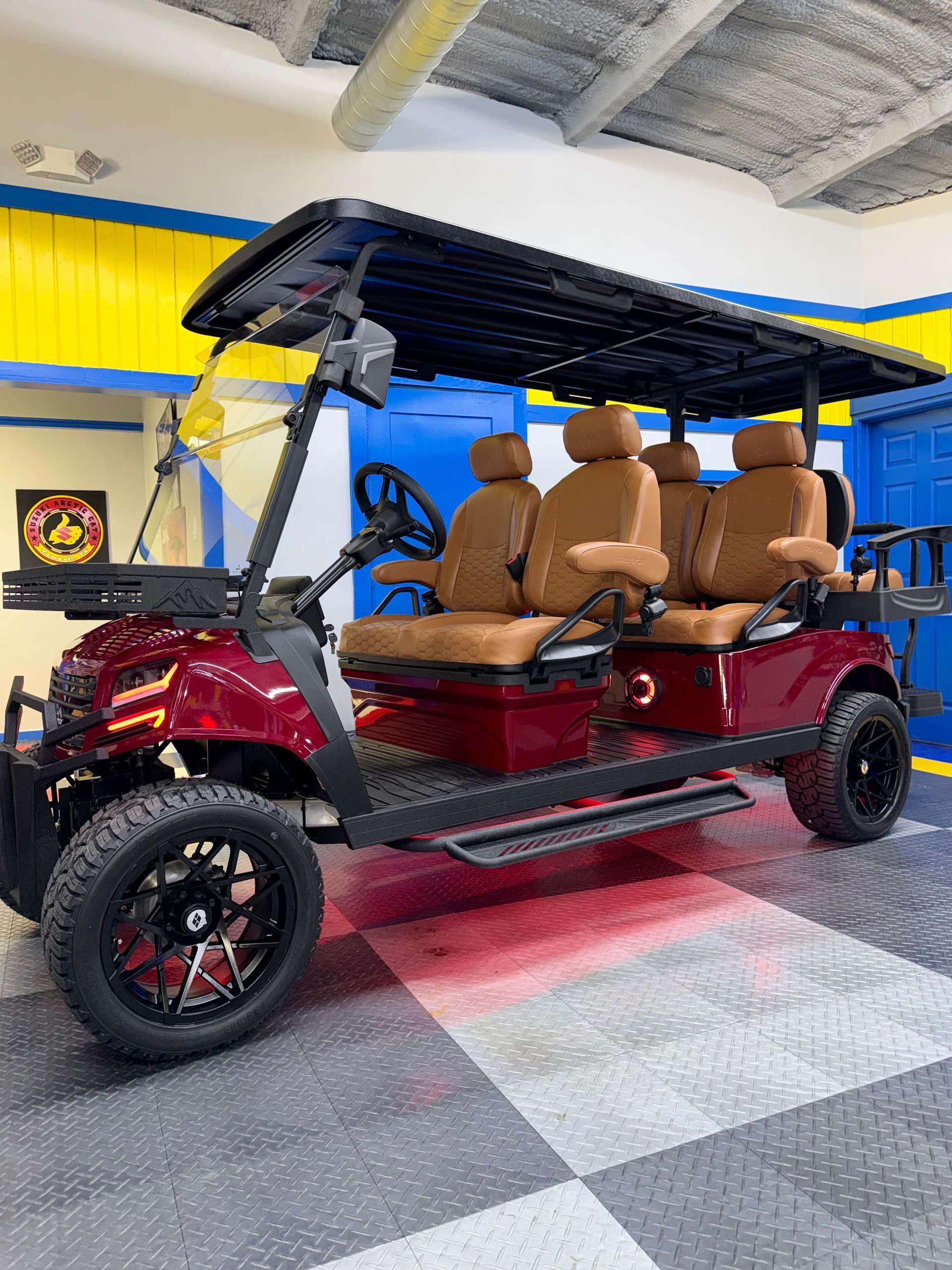 Red electric golf cart with tan seats and black roof displayed indoors on a checkered floor.