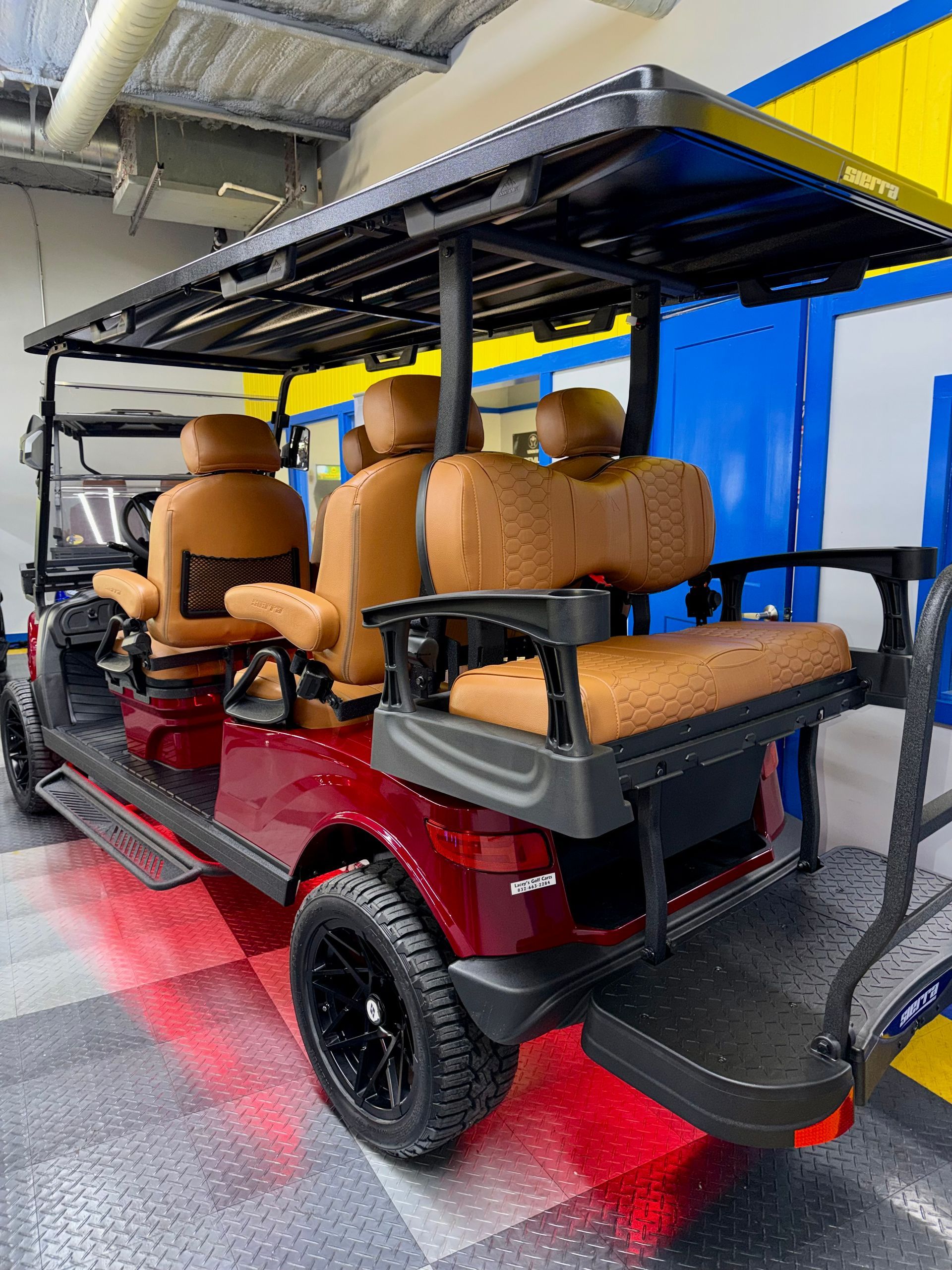 Red golf cart with tan seats and roof parked indoors on a glossy red floor.