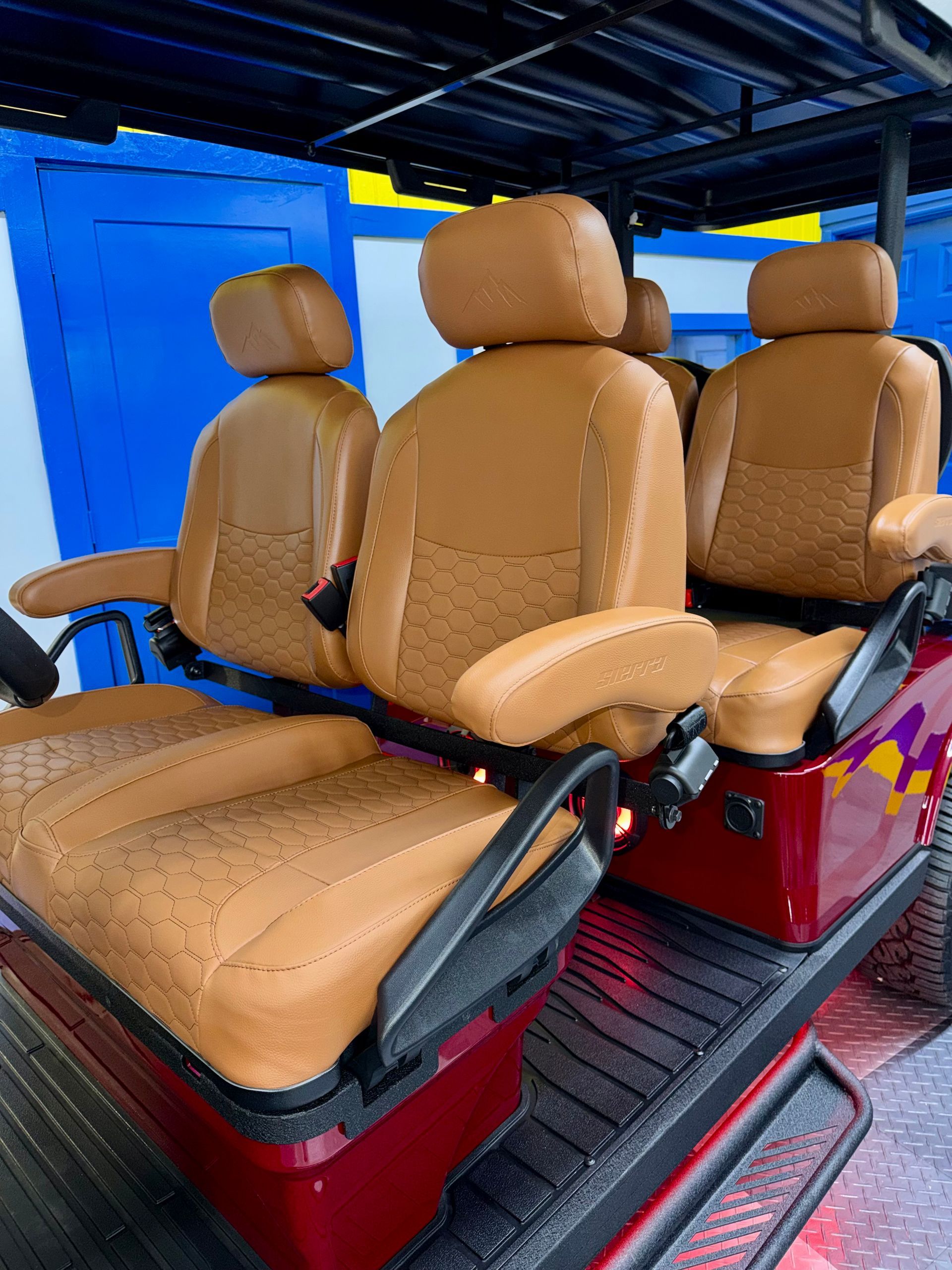 Three tan car seats mounted on a red frame in a blue indoor workshop