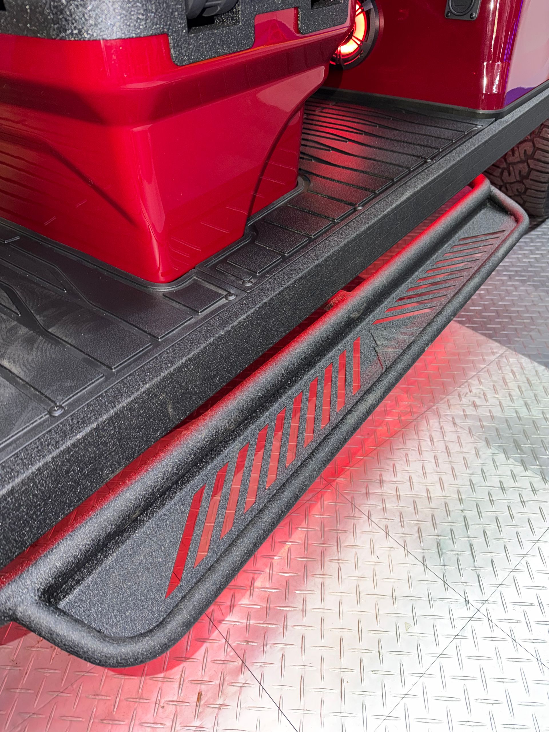 Red industrial machine with a black side step on a diamond-plate metal floor.
