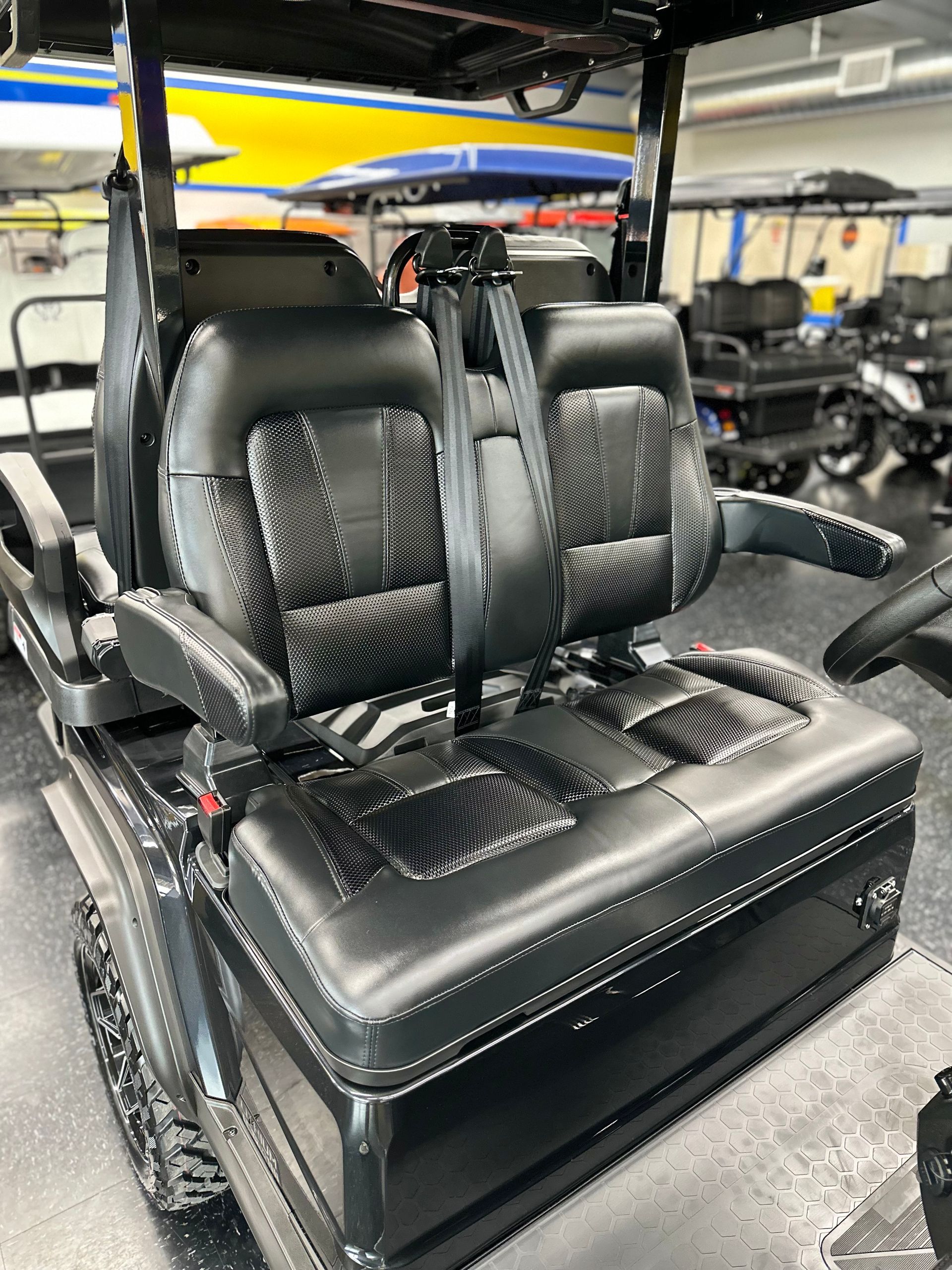 Black golf cart interior with two black, padded seats and armrests. Interior has quilted stitching and a seat belt.