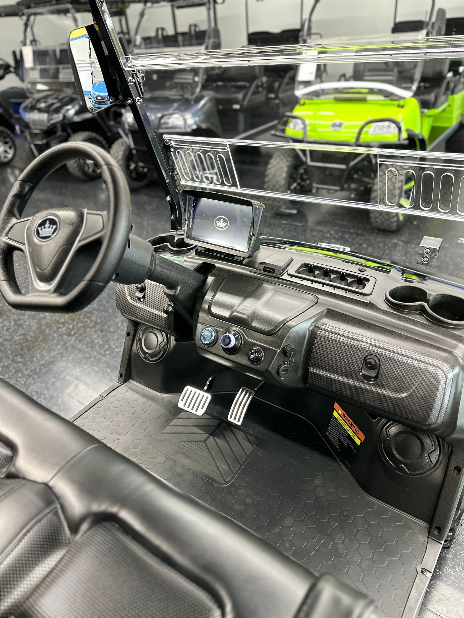 Interior of a black and carbon fiber golf cart with a steering wheel, dashboard, and digital display.