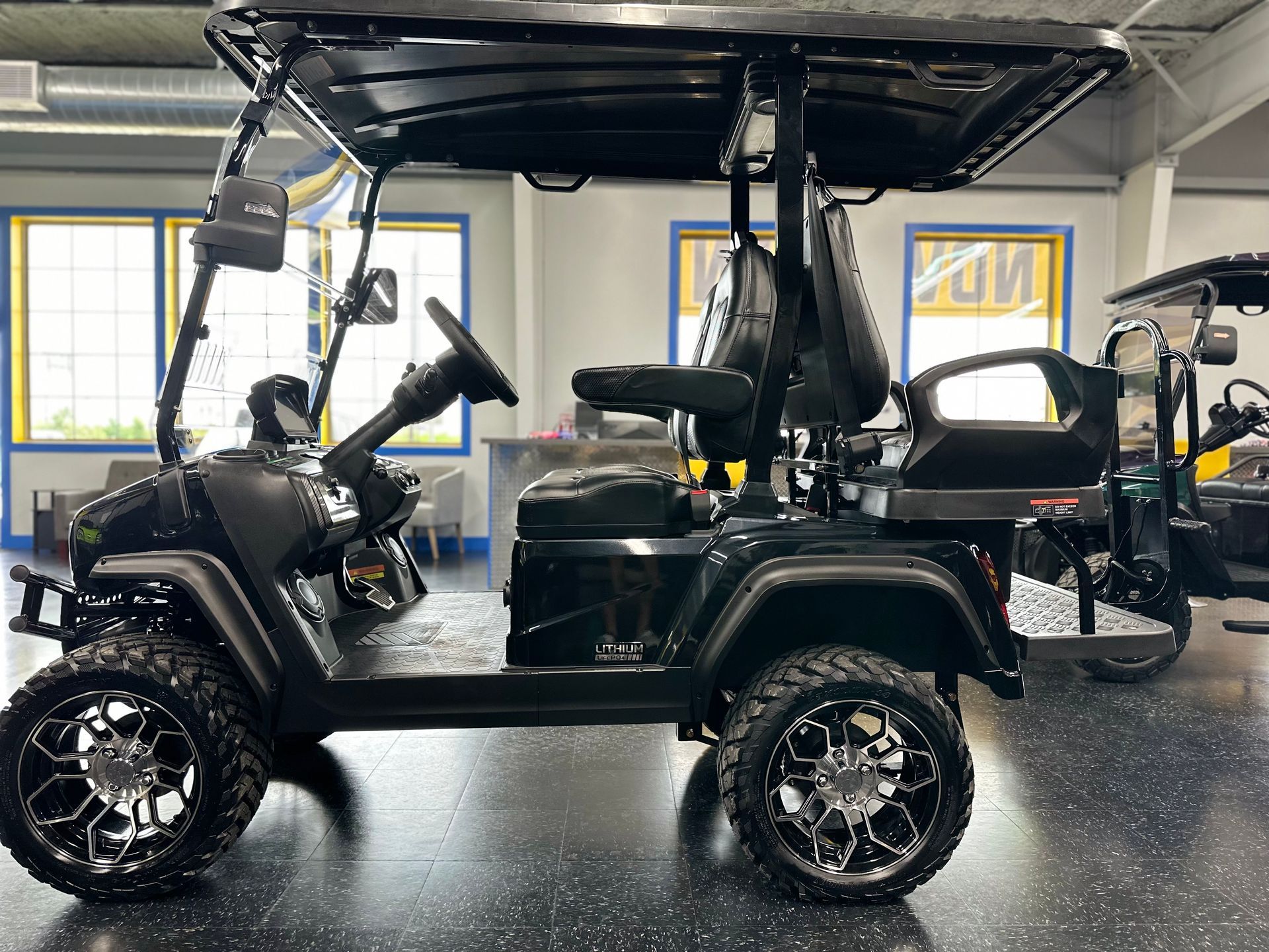 Black golf cart with off-road tires, a canopy, and two rows of seats parked indoors.