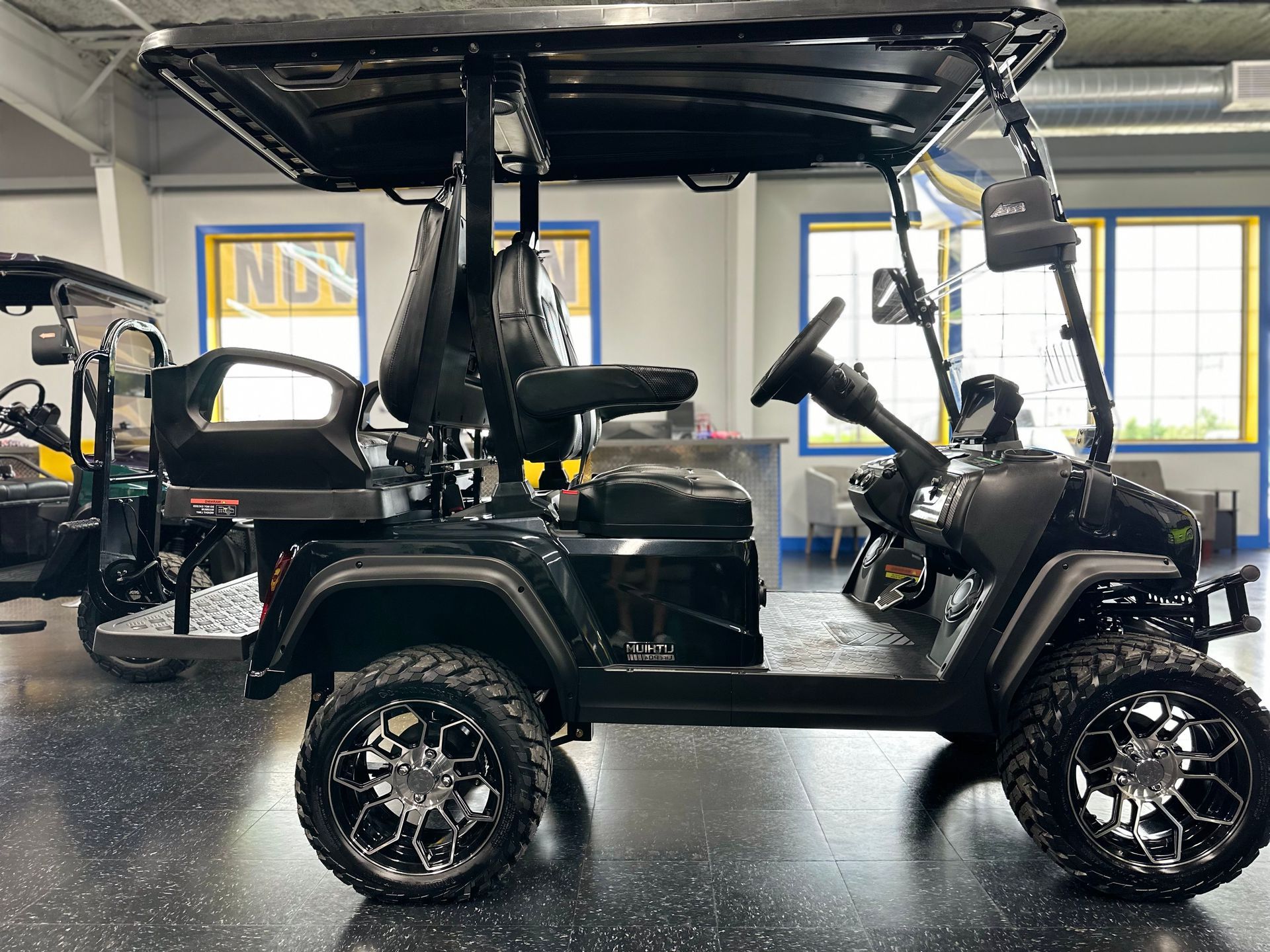Black golf cart with large wheels and a roof in a showroom.
