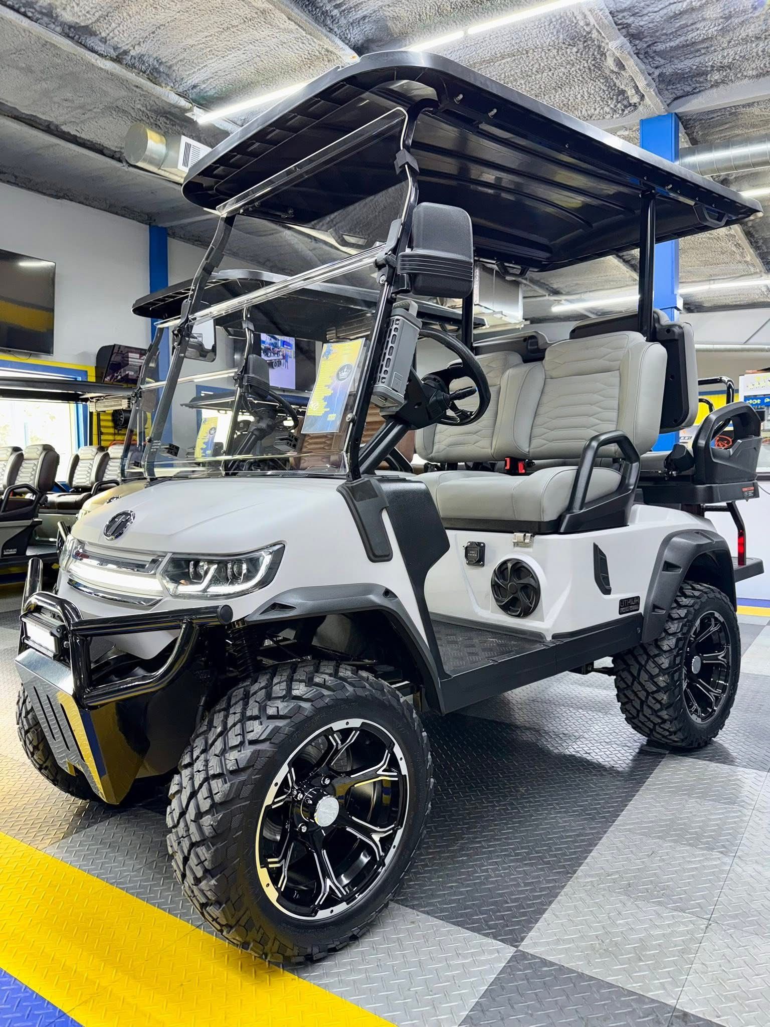 White lifted golf cart with black roof and oversized wheels in a garage or workshop.