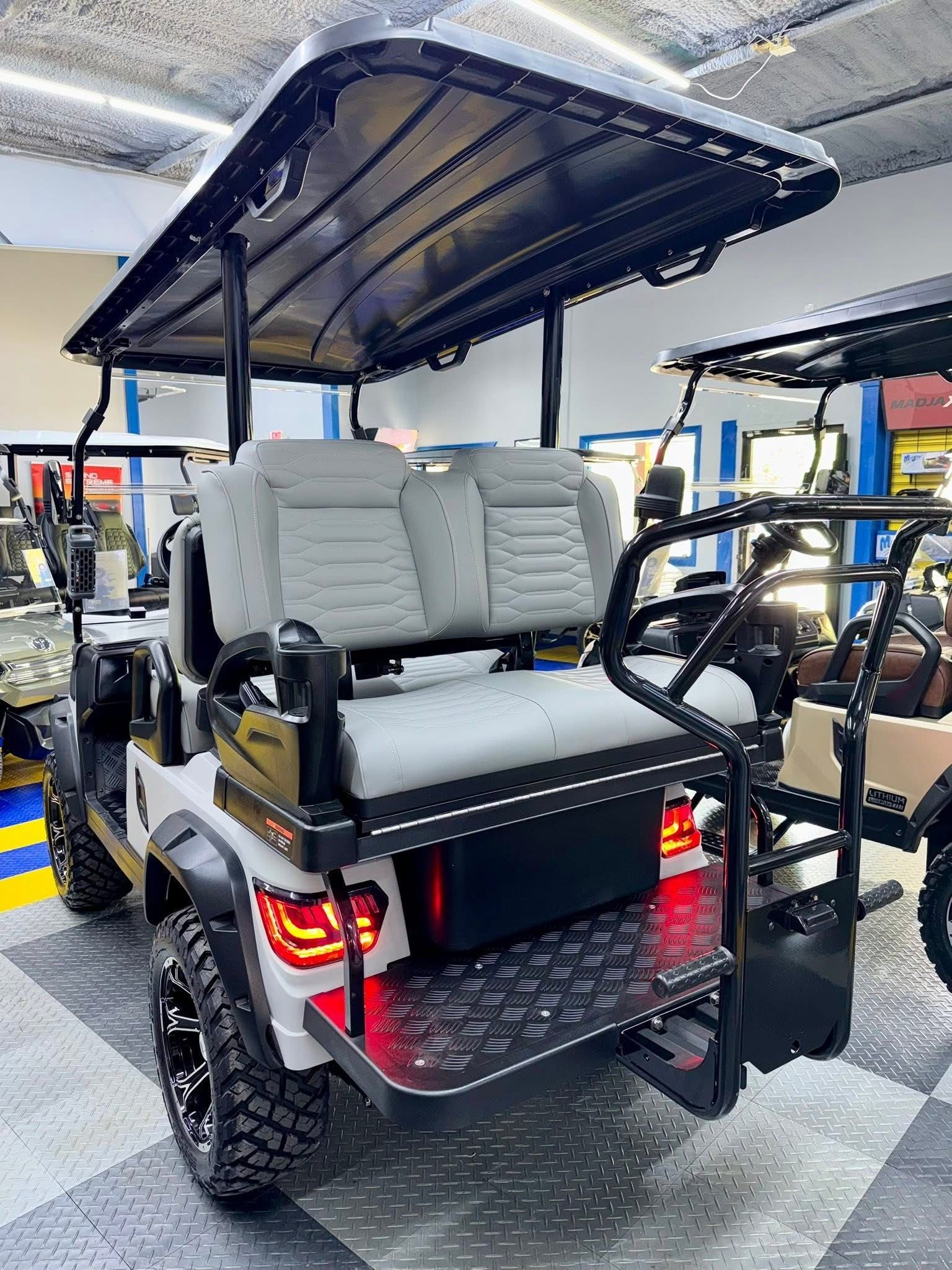 Black golf cart with canopy and beige seats indoors, rear view showing taillights and rugged tires