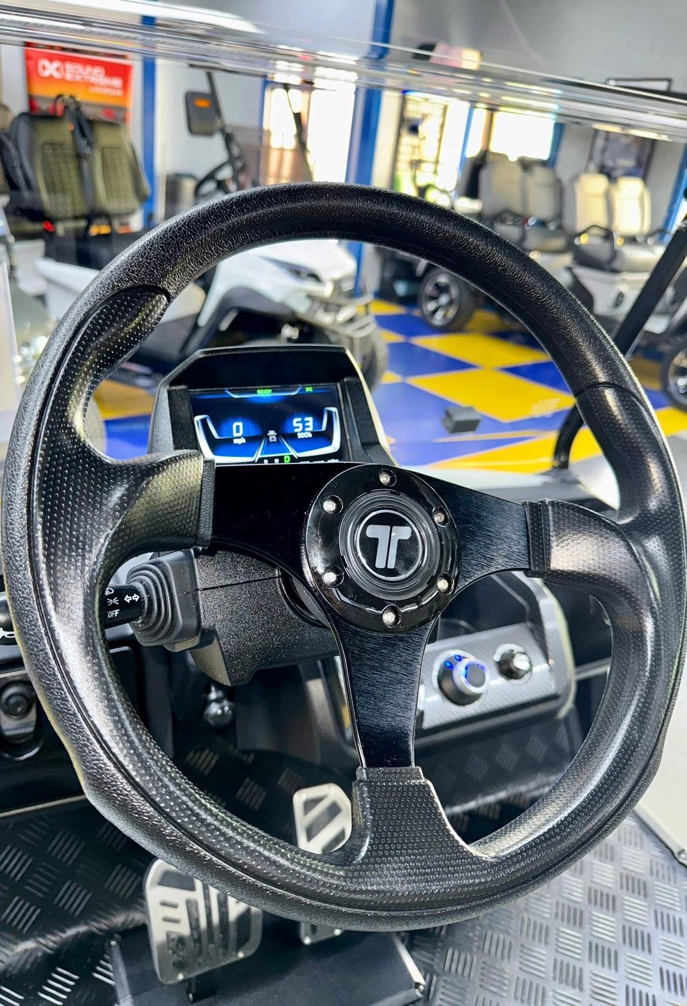 Close-up of a black racing steering wheel controller in an arcade or simulator setup.