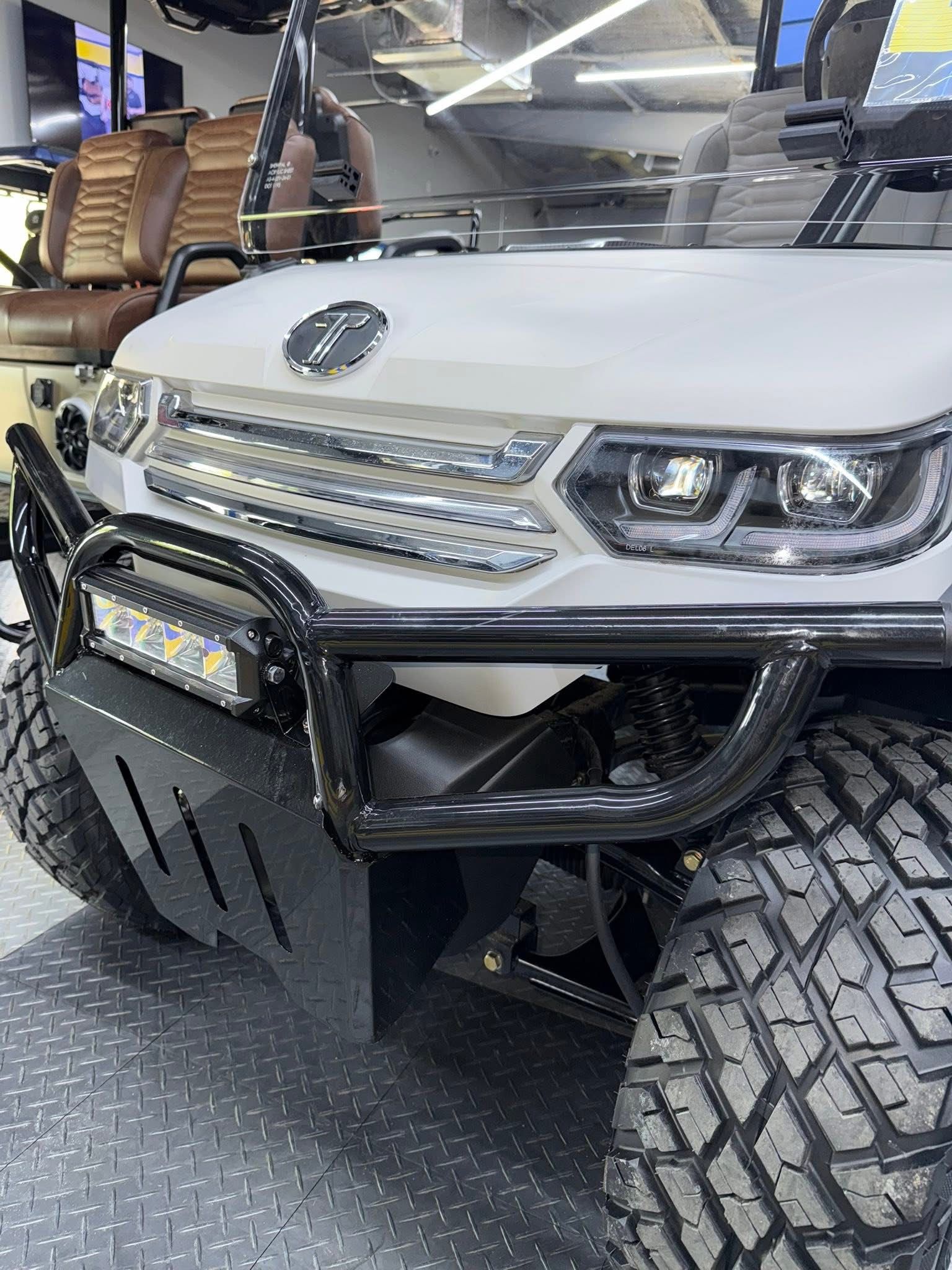 White off-road vehicle front with large tires and bumper in a workshop