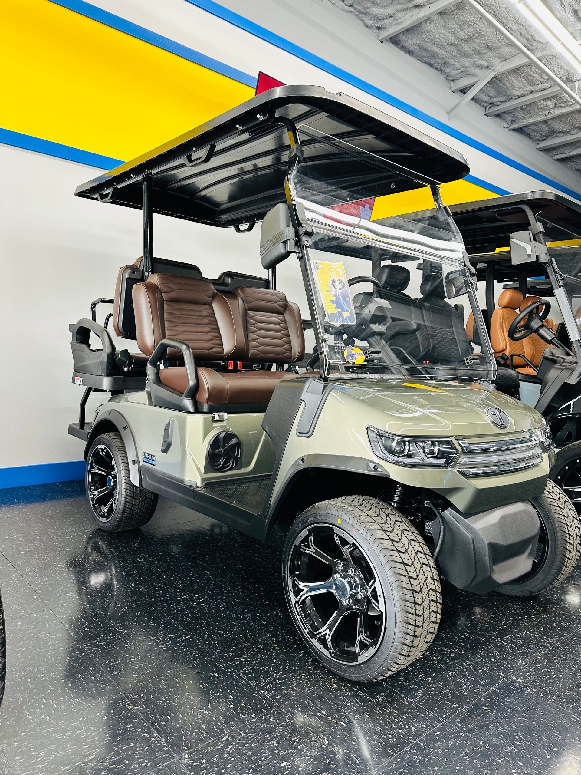 Olive green off-road golf cart with roof canopy parked indoors on a glossy black floor.