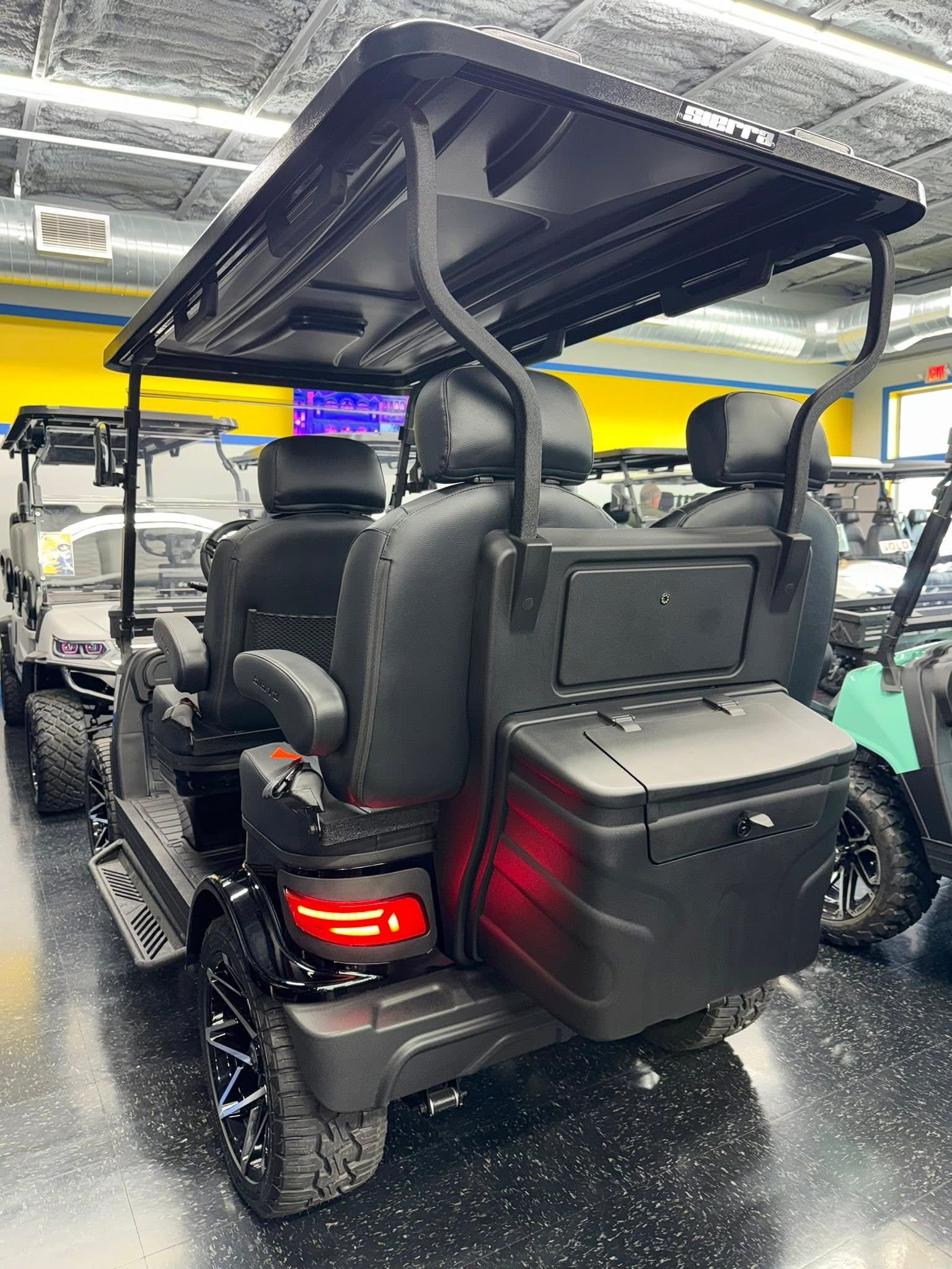 Black golf cart with rear cargo box and roof, parked indoors under bright showroom lights.