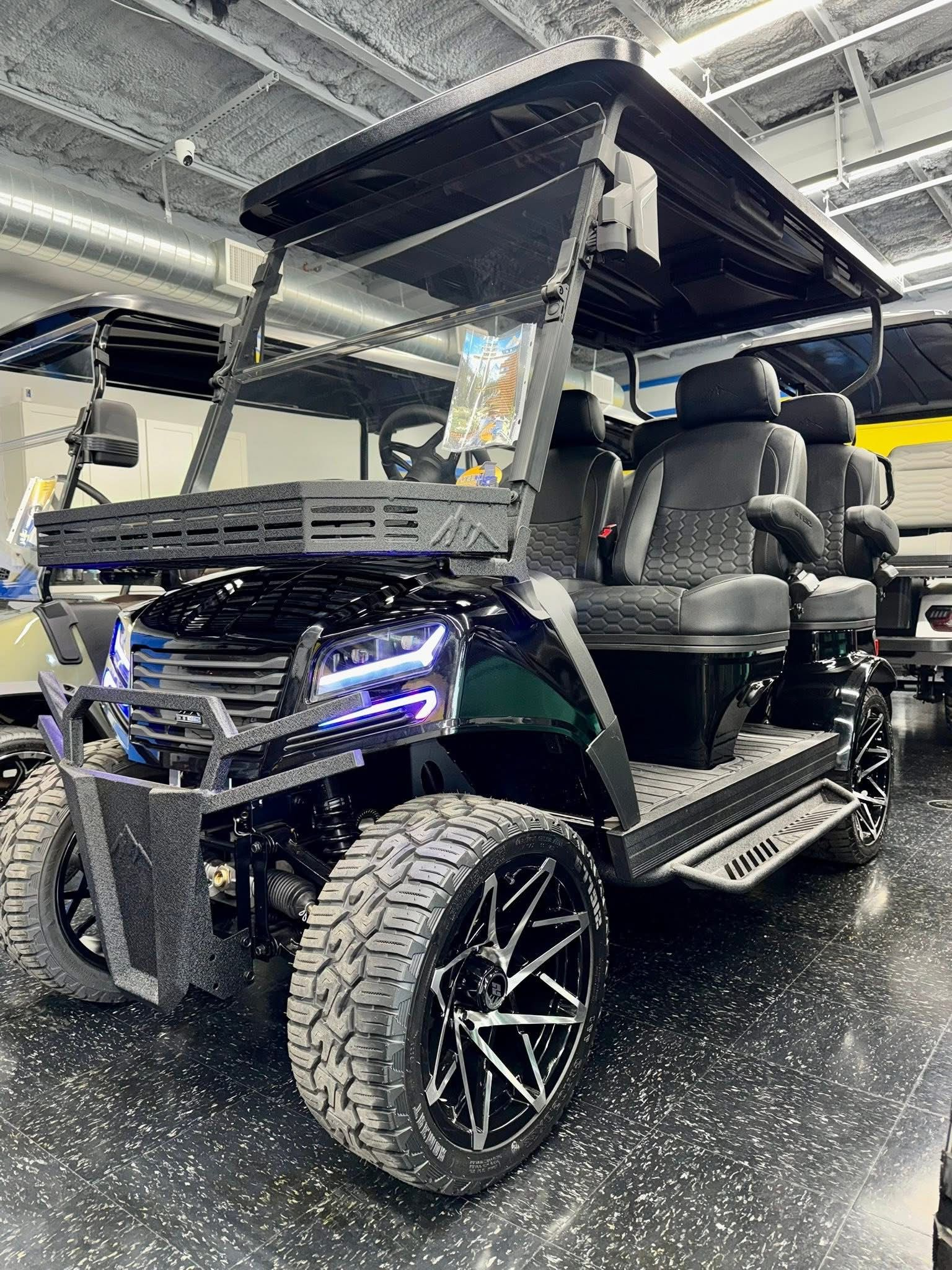 Black custom golf cart with roof and large off-road tires in an indoor showroom