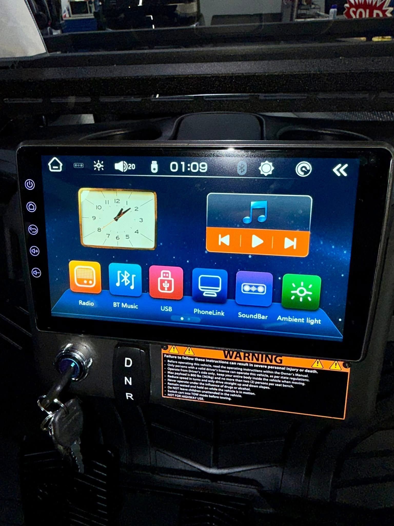 Car dashboard touchscreen showing clock, music, and app icons on a dark car interior console