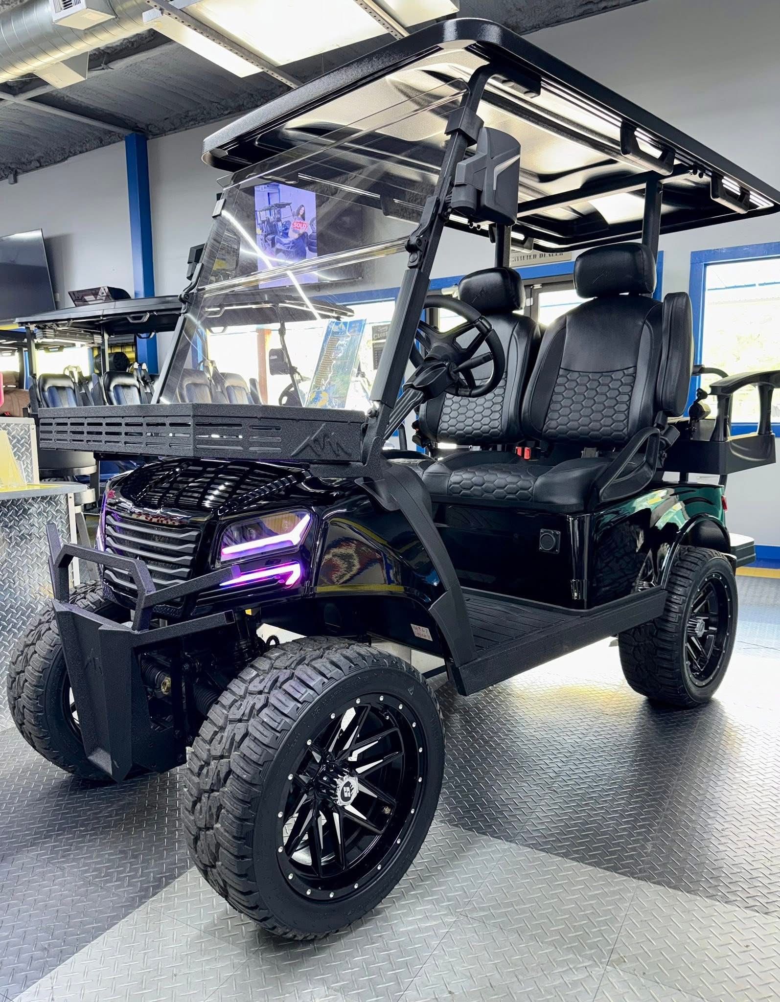 Black off-road golf cart with roof and knobby tires parked indoors under bright lights