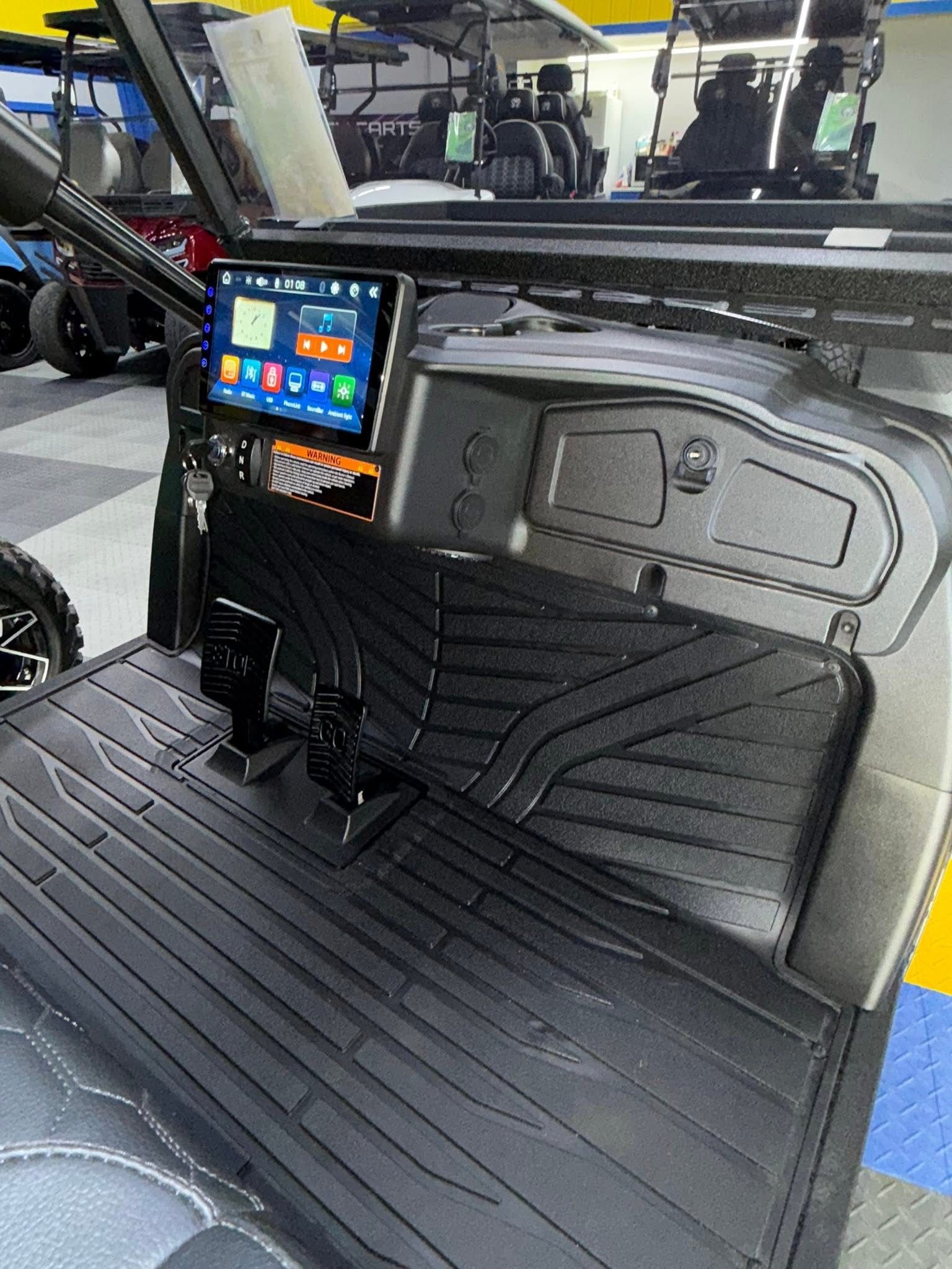 Black utility seat with touchscreen controls in a vehicle interior, with ribbed floor mat and industrial equipment behind it