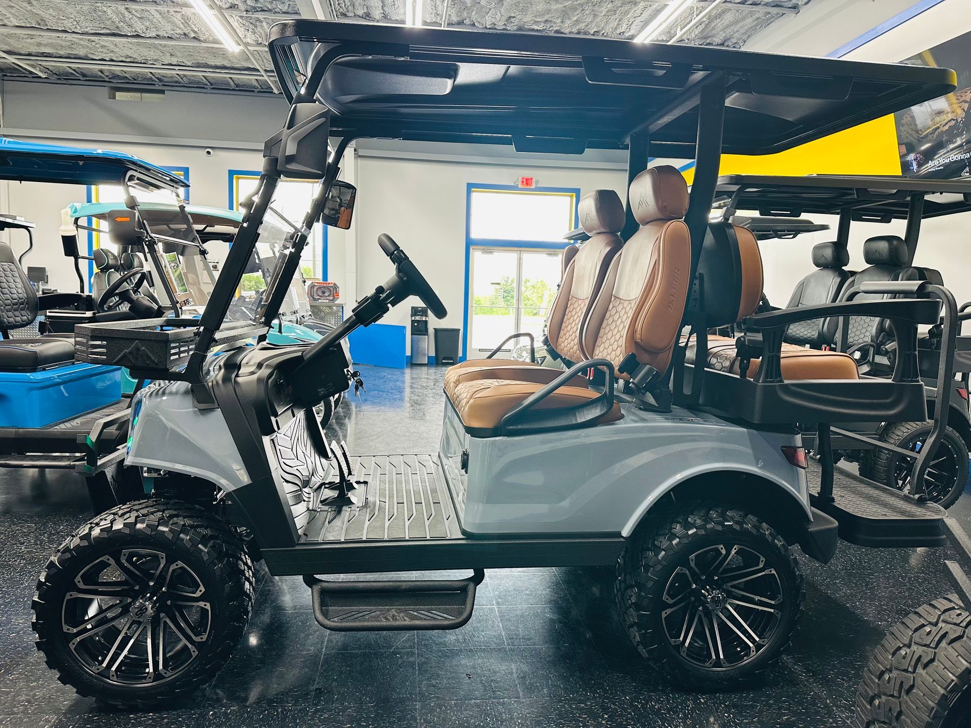 Gray golf cart with tan seats in a showroom, side view with open roof and black wheels
