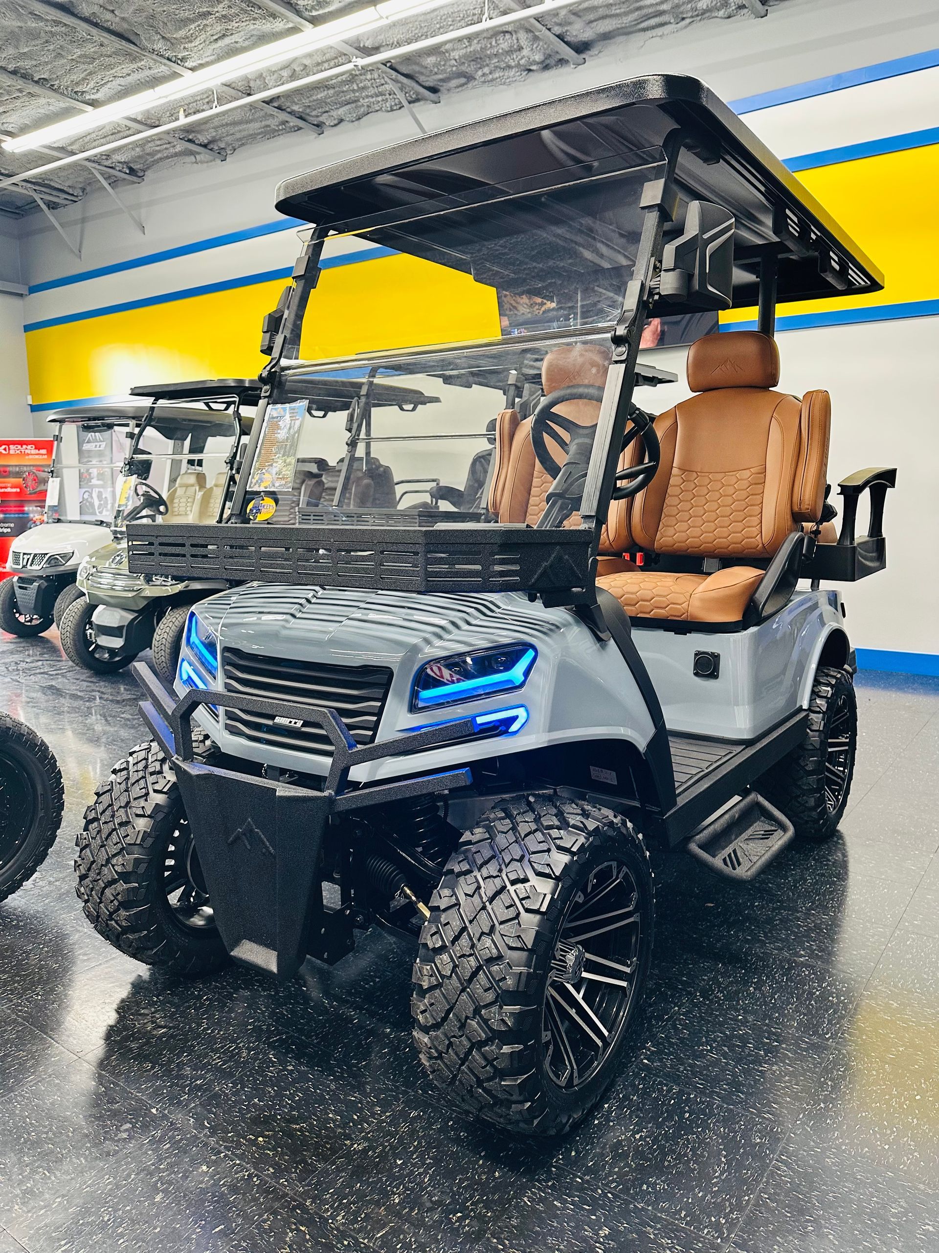 Black-and-white utility golf cart with tan seats, blue headlights, and roof display in a showroom