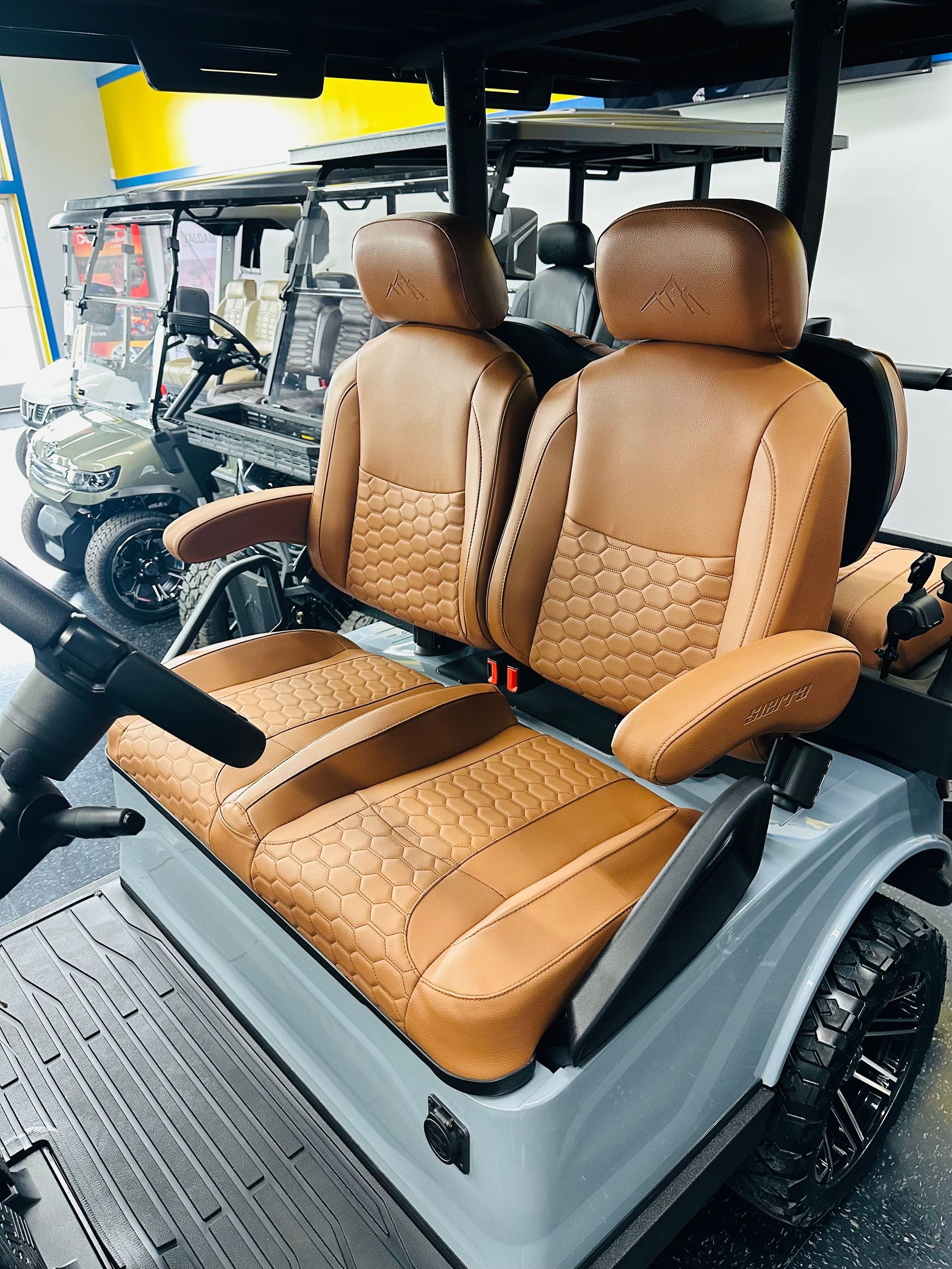 Tan upholstered golf cart seat with matching backrests and armrests on a black cart frame.