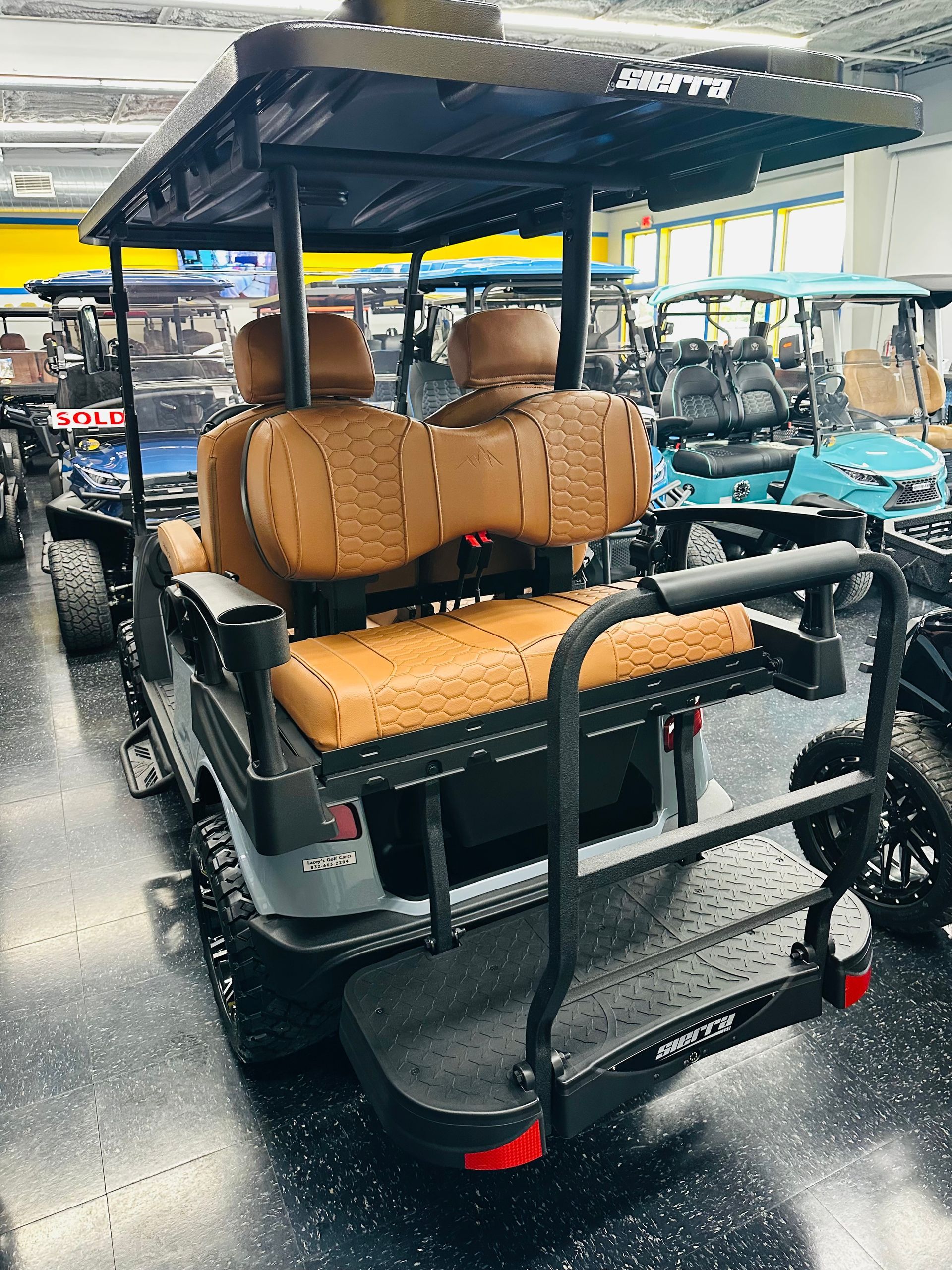 Black utility golf cart with tan seats and roof in an indoor showroom under bright lights.