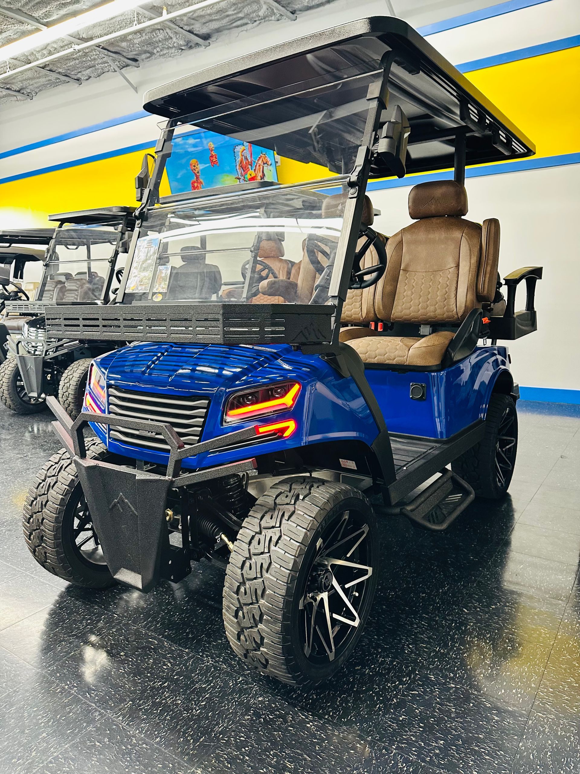 Blue off-road golf cart with tan seats and roof, shown indoors on a wet, reflective floor.