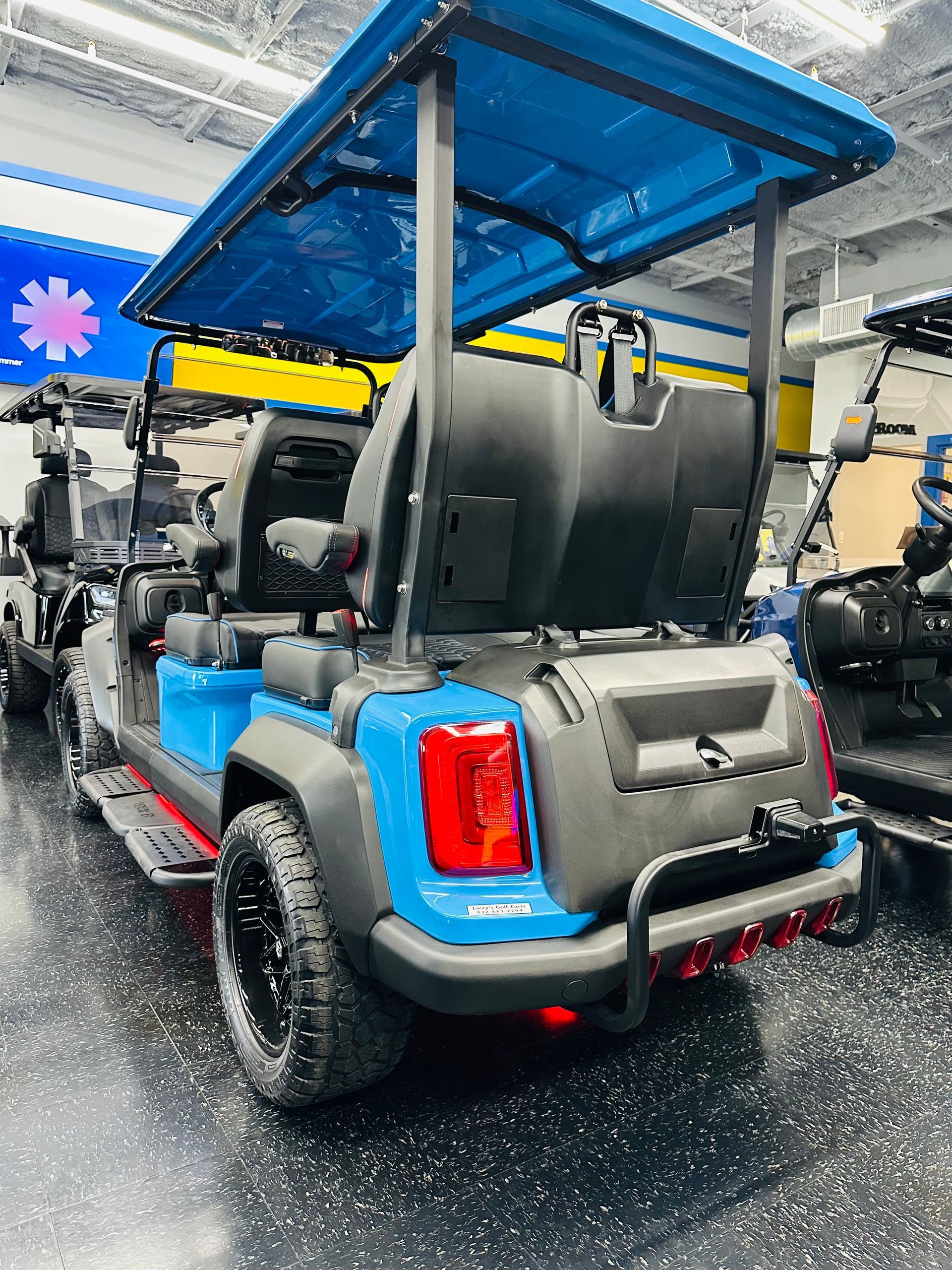 Blue-roofed electric golf cart with black seats and red taillight, parked indoors on a wet floor.