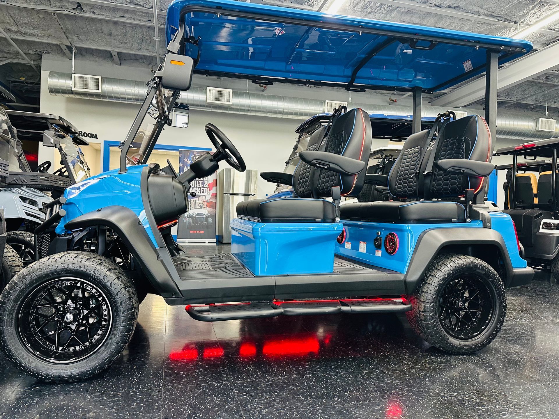 Blue golf cart with four seats, black off-road wheels, and red underglow parked in a garage.
