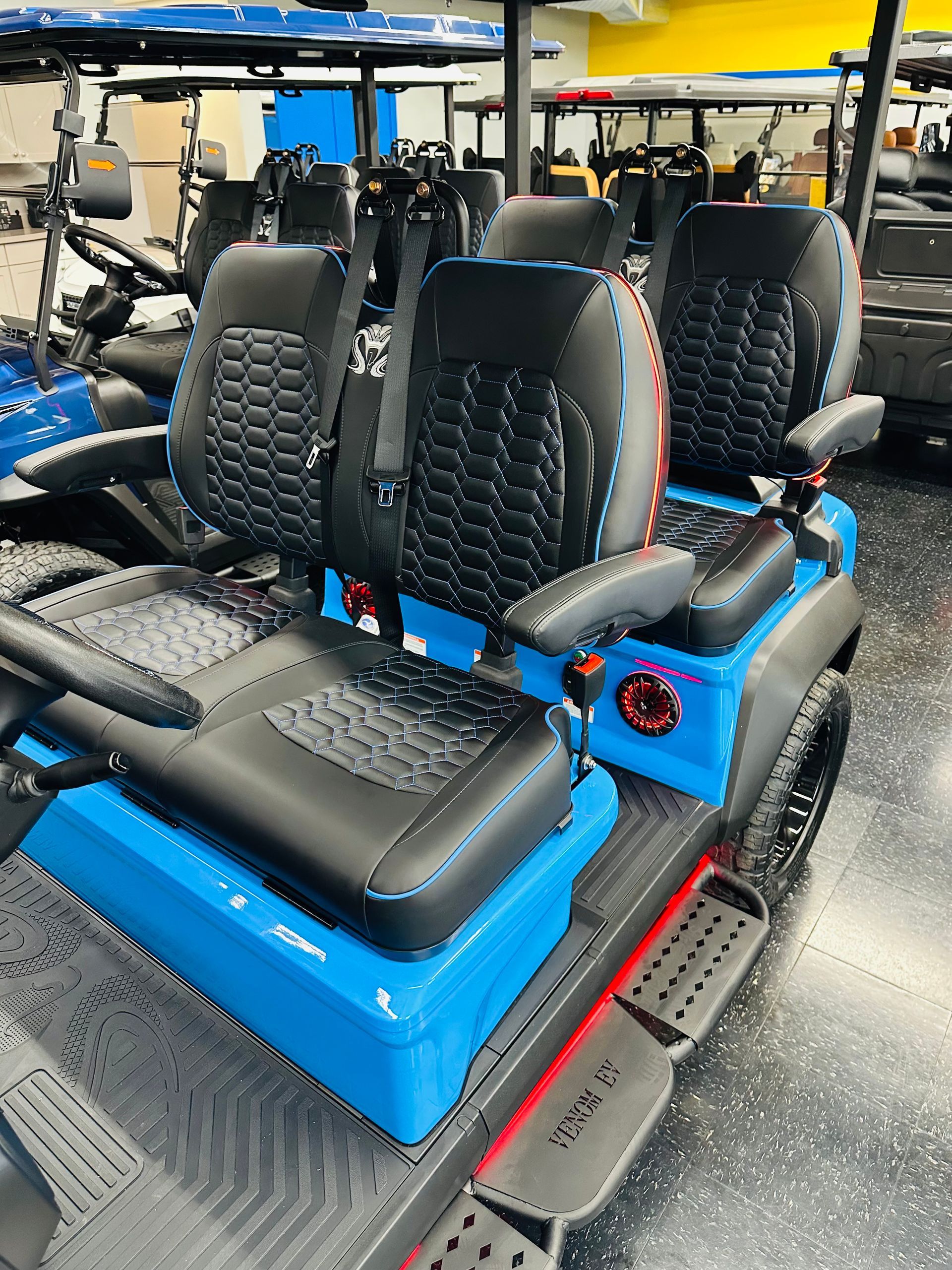 Bright blue off-road golf cart with black seats and large tires in a showroom