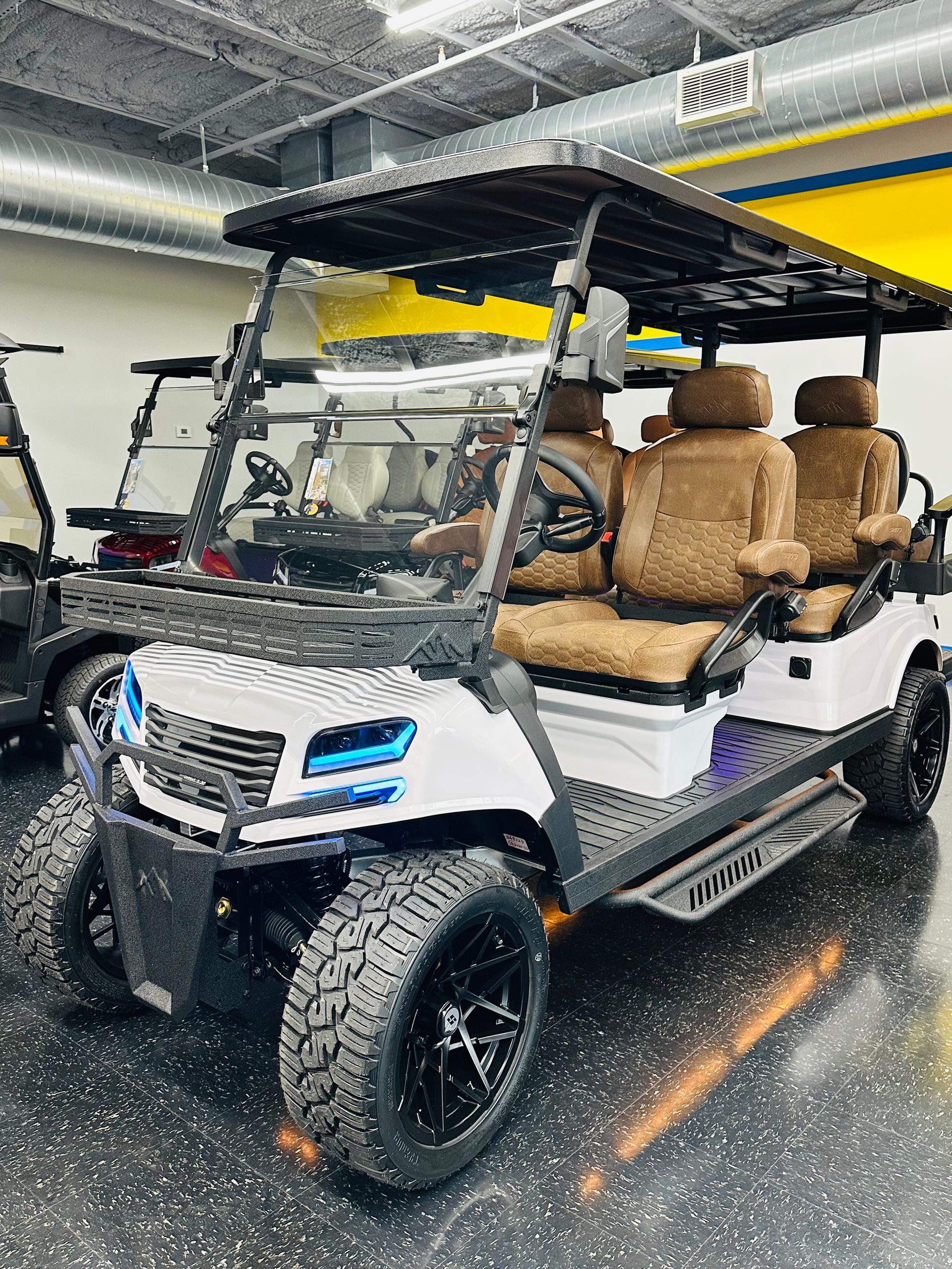 White golf cart with tan seats parked indoors on a wet floor under a roofed structure