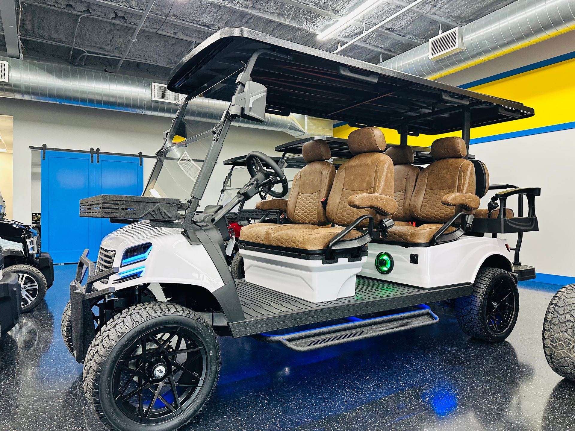 White golf cart with tan seats and black canopy, shown indoors under bright showroom lights.