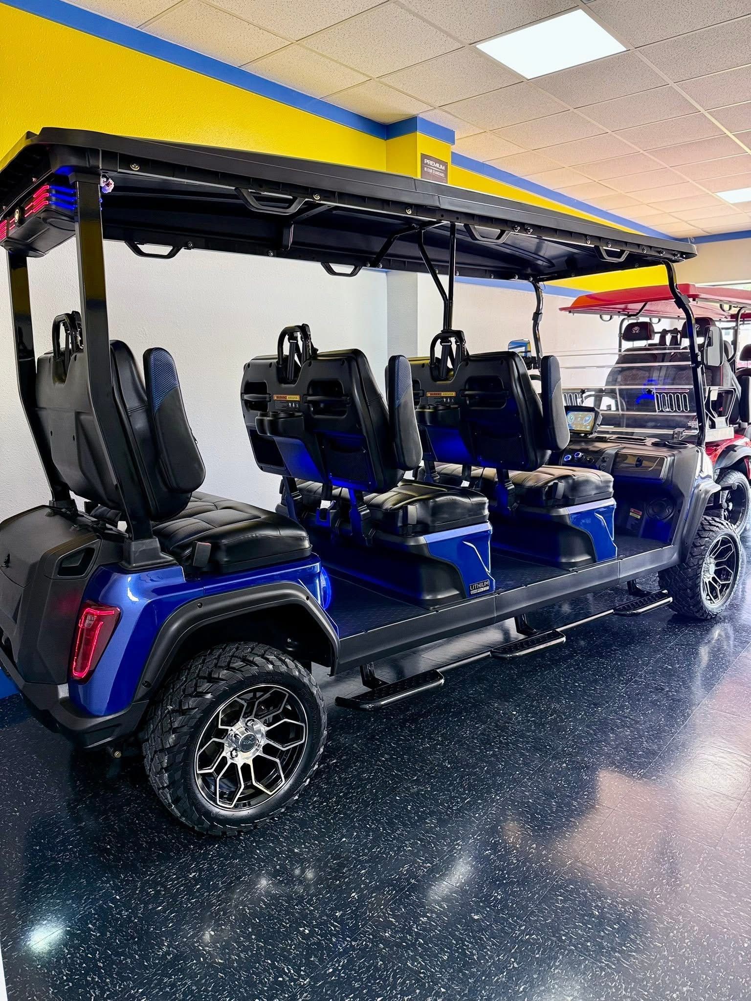 Blue multi-seat golf cart parked indoors on a glossy showroom floor under bright lights