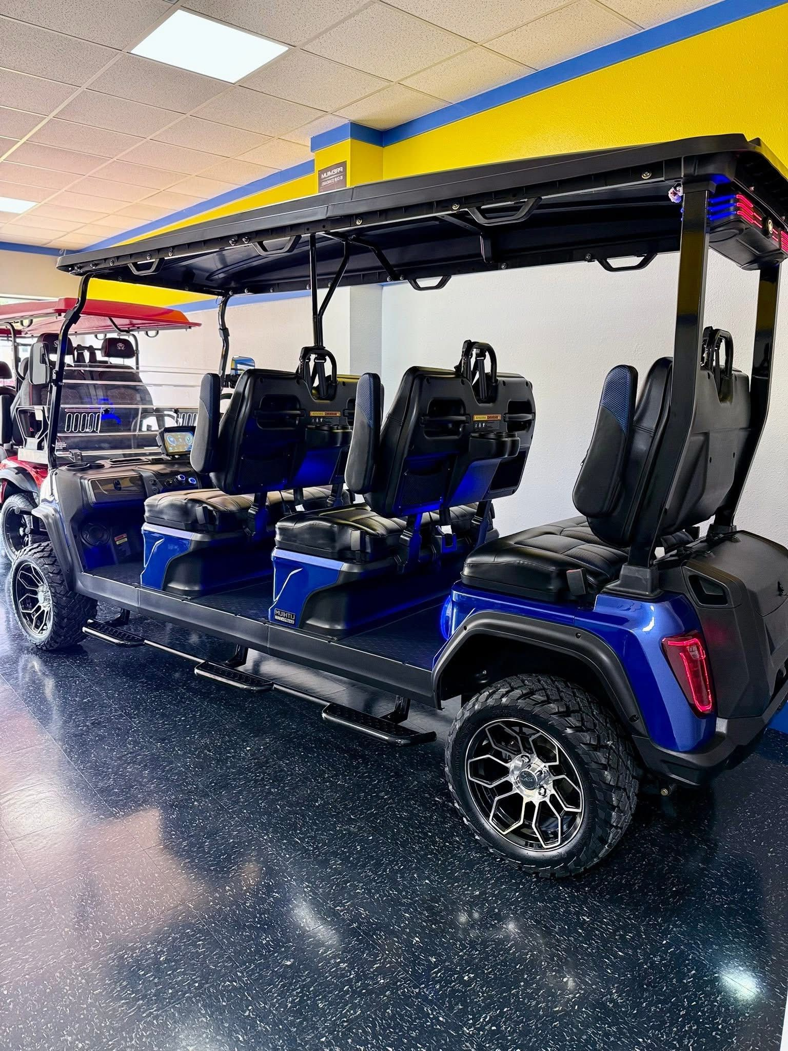 Blue golf cart with yellow roof and black seats displayed indoors on a showroom floor.