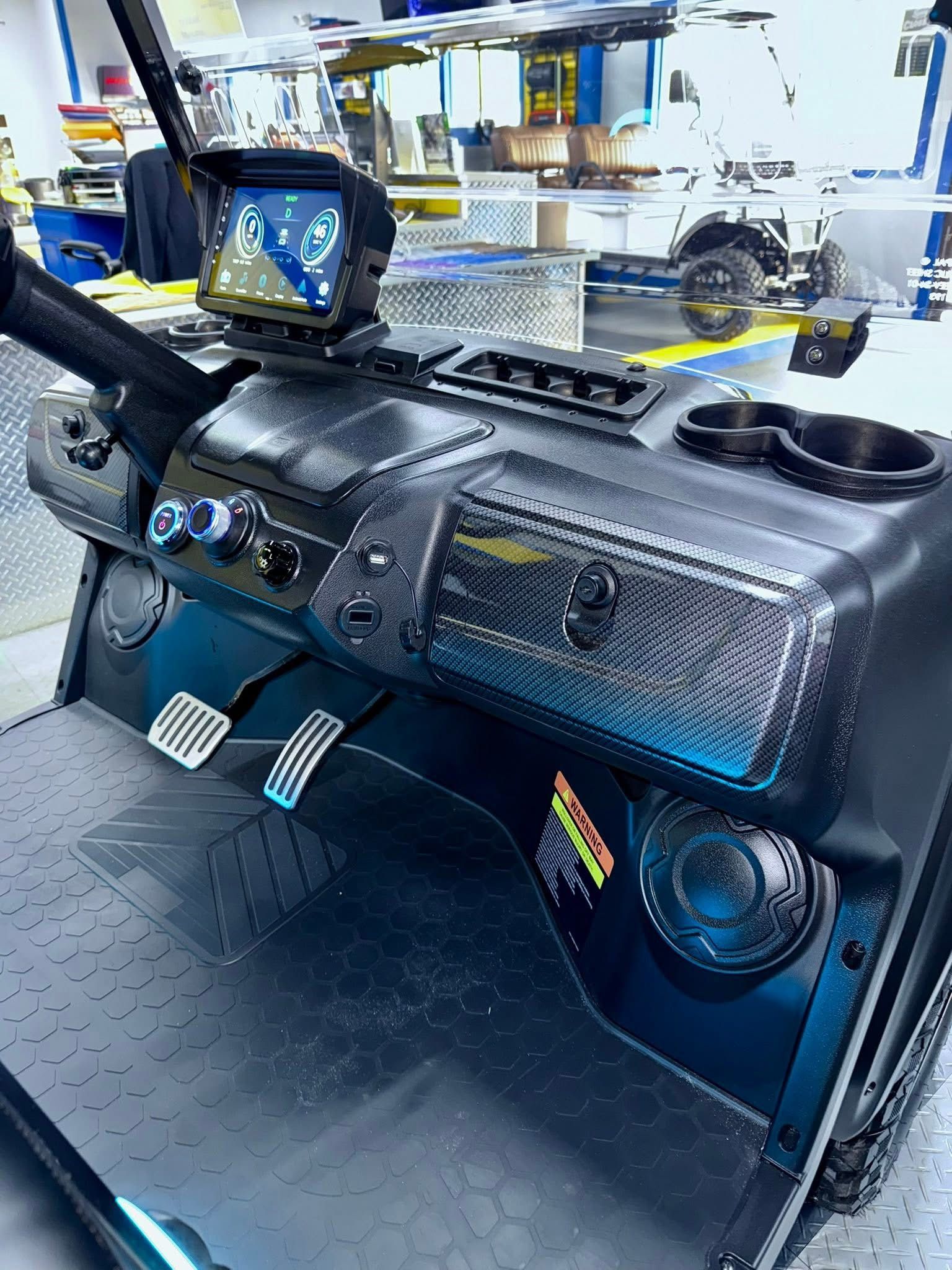 Car dashboard with carbon-fiber-style trim, steering wheel, and digital gauge cluster in a workshop.