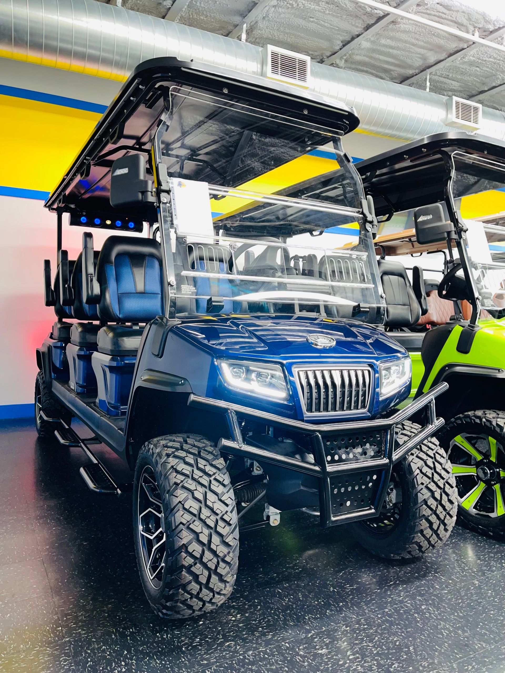 Blue golf cart with roof and large tires displayed indoors under bright showroom lights