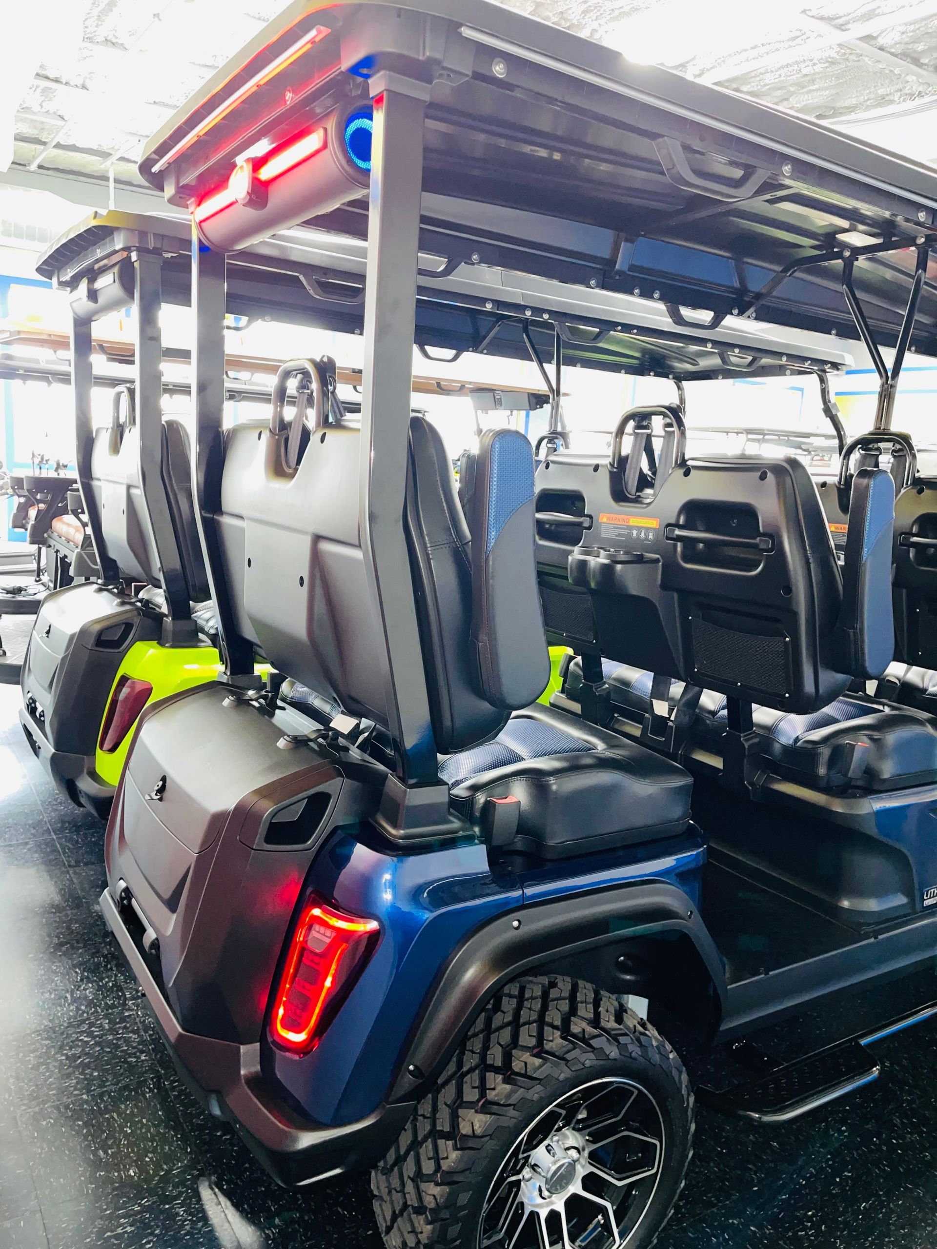 Blue golf cart with roof lights and tan seats, shown from the rear in a garage or showroom.