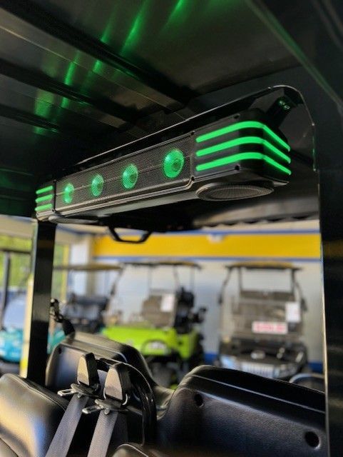 Green LED light bar mounted on a golf cart roof, illuminating the interior. Other golf carts are in the background.